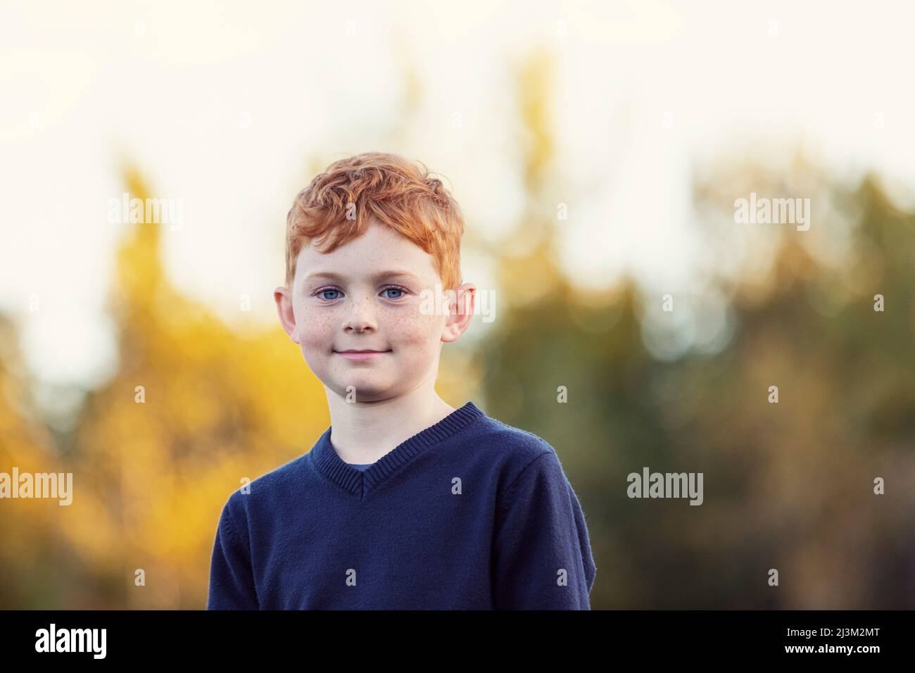 Outdoor portrait of boy with red hair and freckles and blurred autumn colours in the background; Edmonton, Alberta, Canada Stock Photo