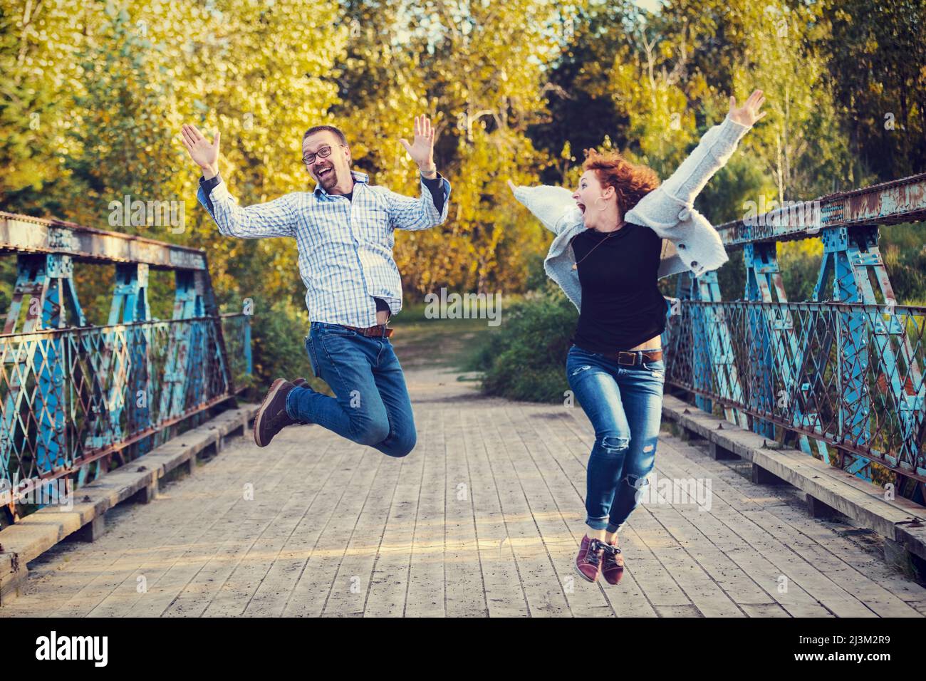 Mature married couple outside in a park leaps in mid-air in exuberant celebration; Edmonton, Alberta, Canada Stock Photo