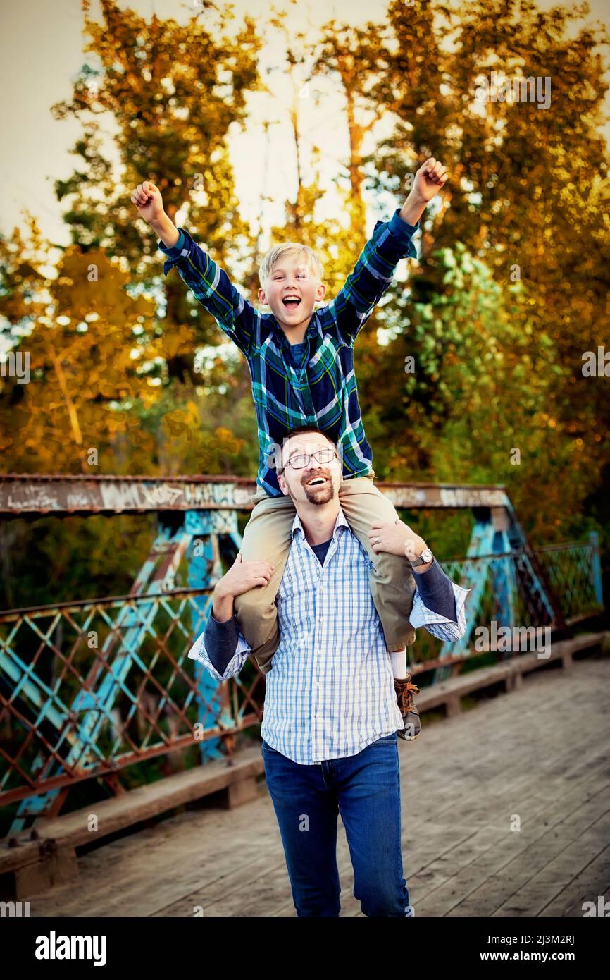 Father giving his son a shoulder ride in a park in autumn; Edmonton, Alberta, Canada Stock Photo
