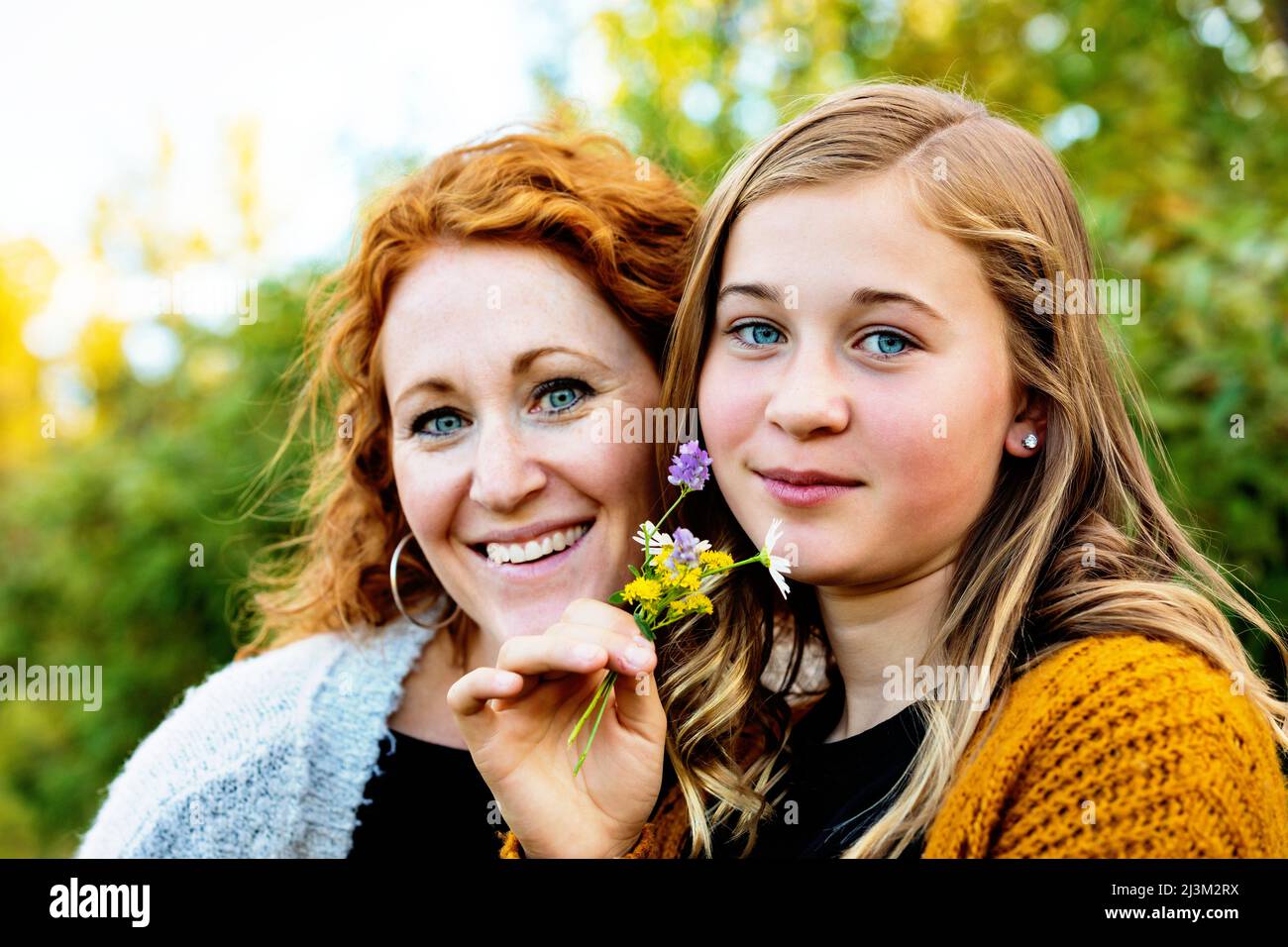 Outdoor portrait of a mother with her teenage girl holding a small cluster of colourful wildflowers and looking at the camera Stock Photo