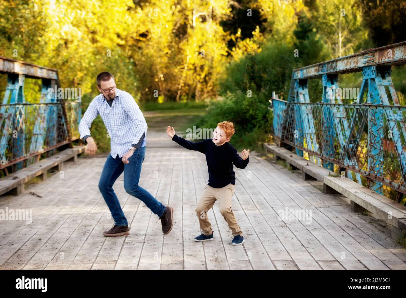 Father and son doing dance moves on a bridge in a park in autumn; Edmonton, Alberta, Canada Stock Photo