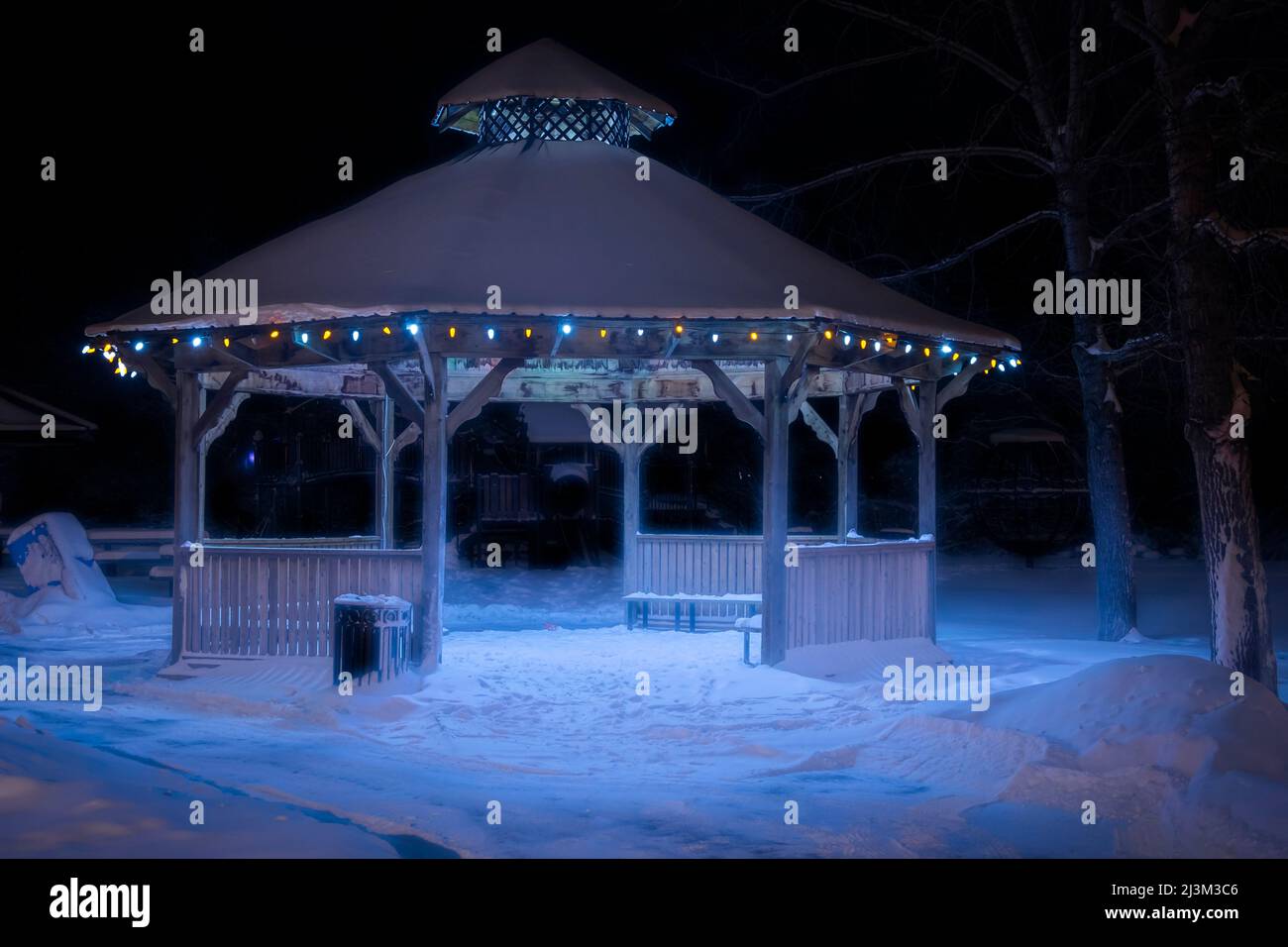 Christmas lights illuminate a gazebo at night in a snowy park in winter
