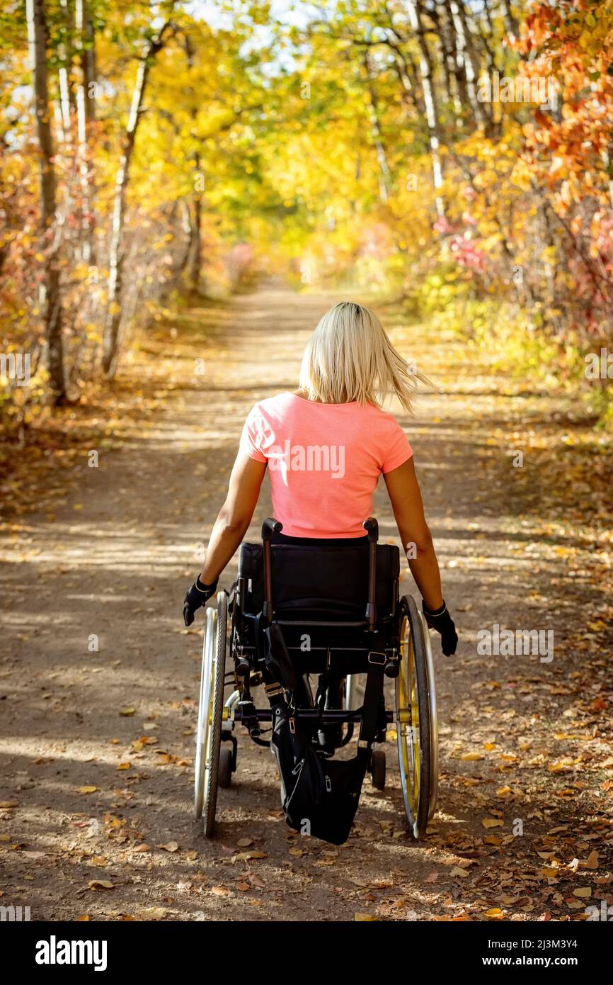 Young paraplegic woman in her wheelchair going down a trail in a park on a beautiful fall day