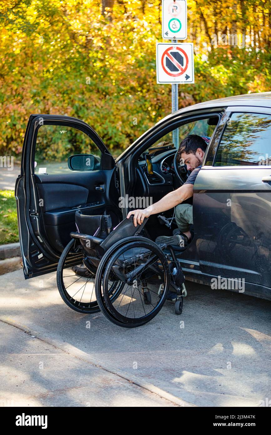 Young paraplegic man moves from his wheelchair to the driver's seat of a car; Edmonton, Alberta, Canada Stock Photo