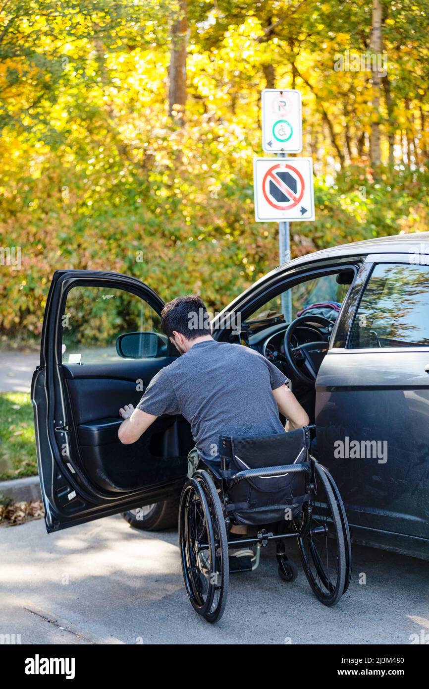 Young paraplegic man moves from his wheelchair to the driver's seat of a car; Edmonton, Alberta, Canada Stock Photo