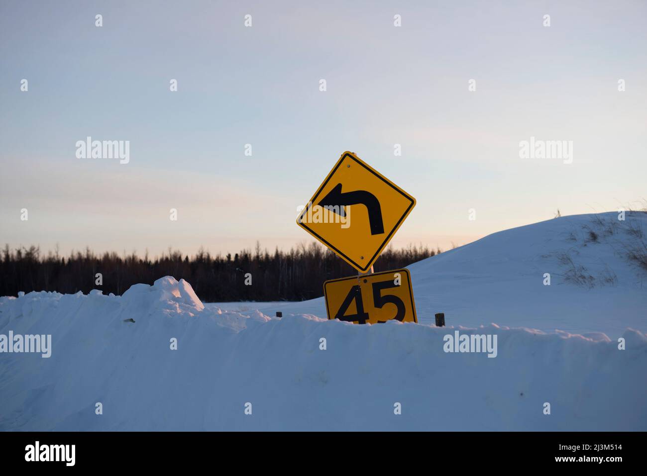 Yellow caution speed limit road sign buried in a deep snowbank; Alberta, Canada Stock Photo