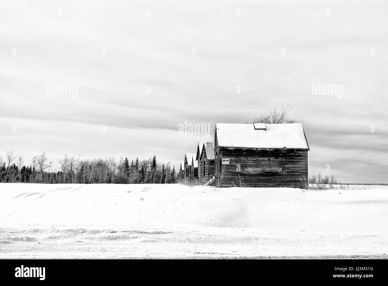 Weathered wooden buildings in a row across a snowy countryside during
