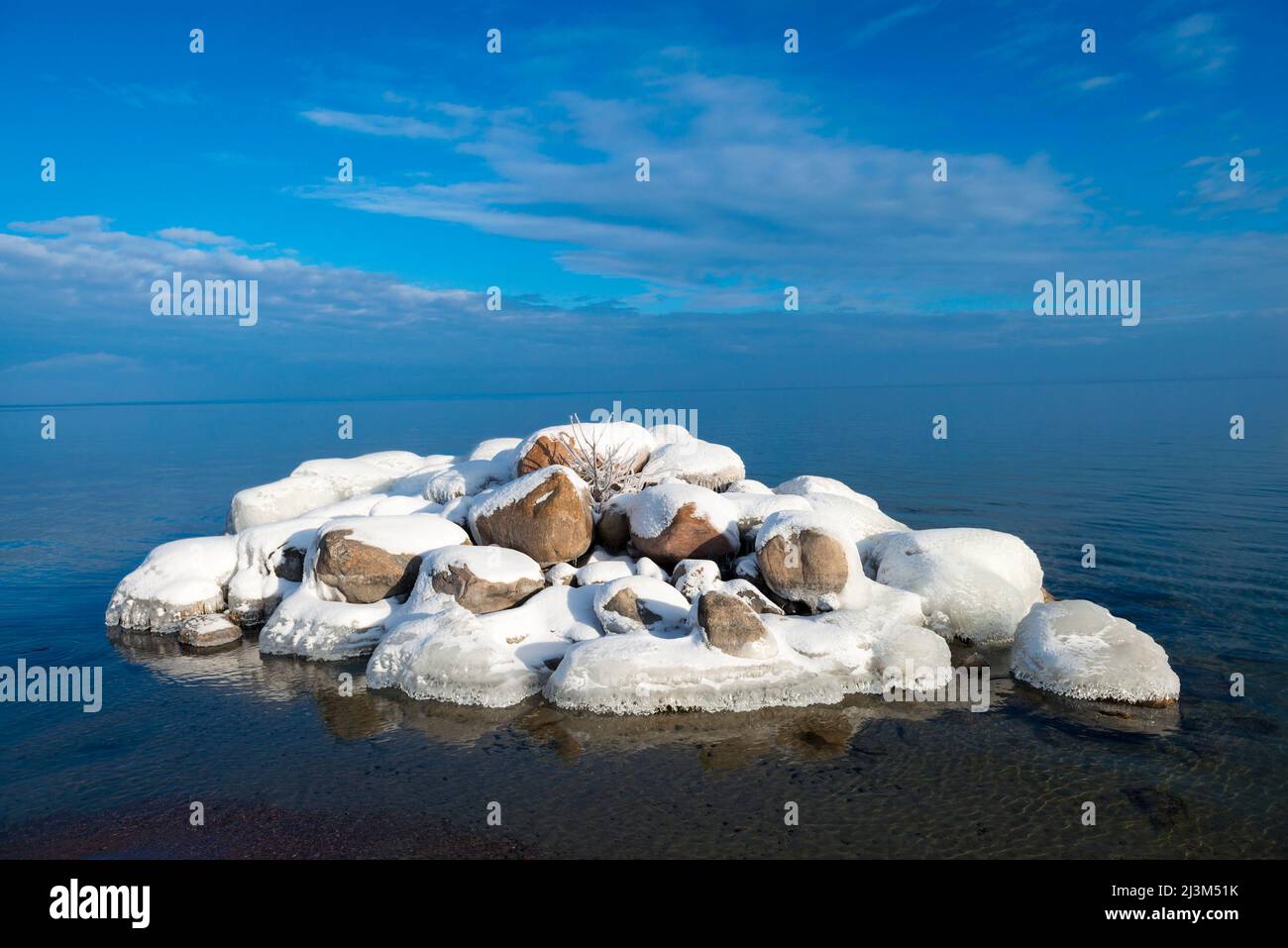 Snowcovered rock pile surrounded by water with clouds over the distant