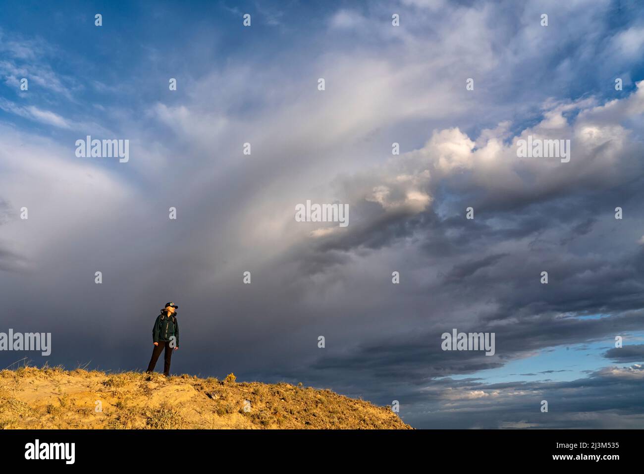 Dramatic cloud formation in the sky behind a woman on a ridge in Grasslands National Park, Saskatchewan, Canada; Val Marie, Saskatchewan, Canada Stock Photo