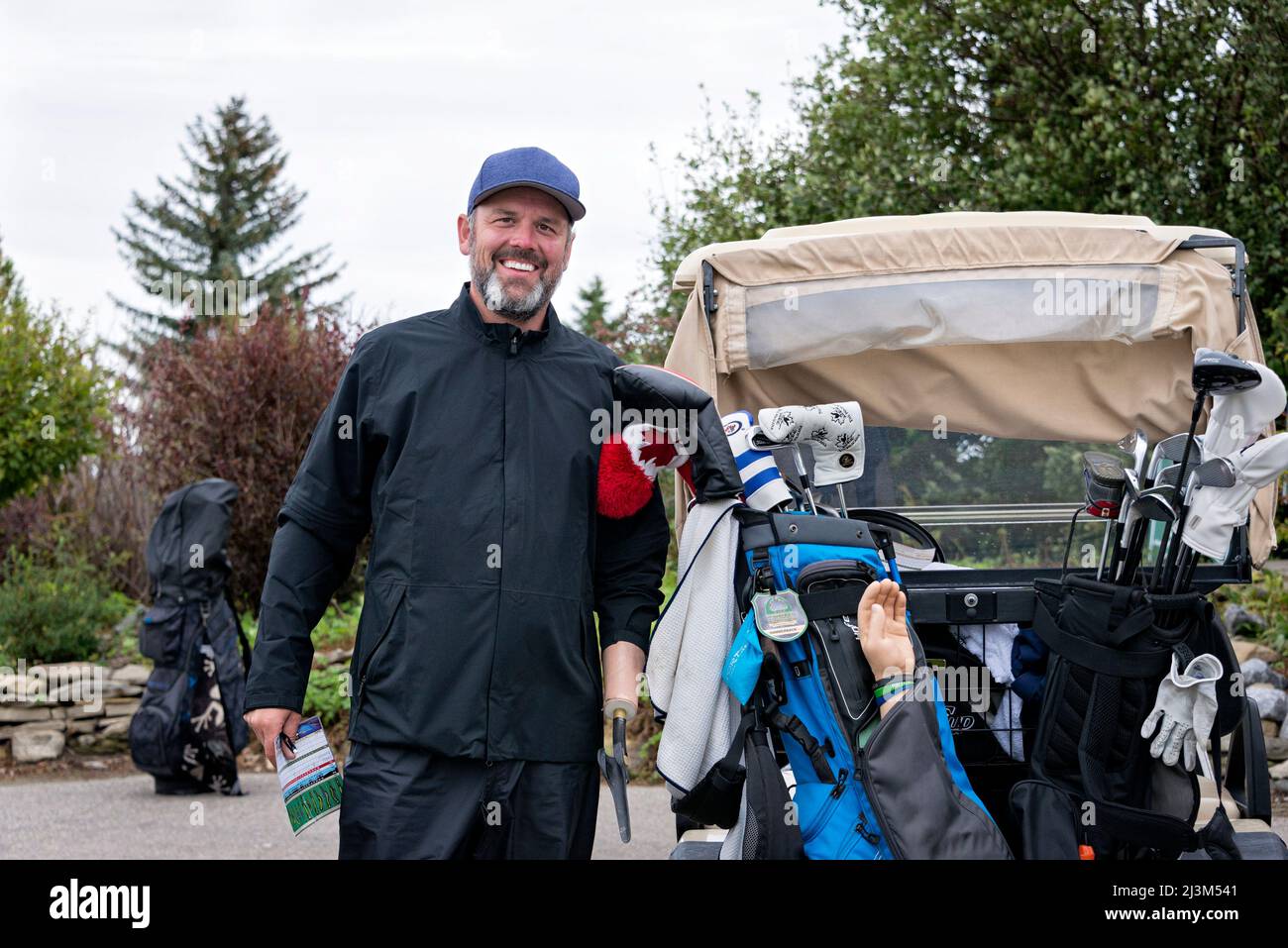 Golfer with arm prothesis standing beside a golf cart at a golf course; Okotoks, Alberta, Canada Stock Photo