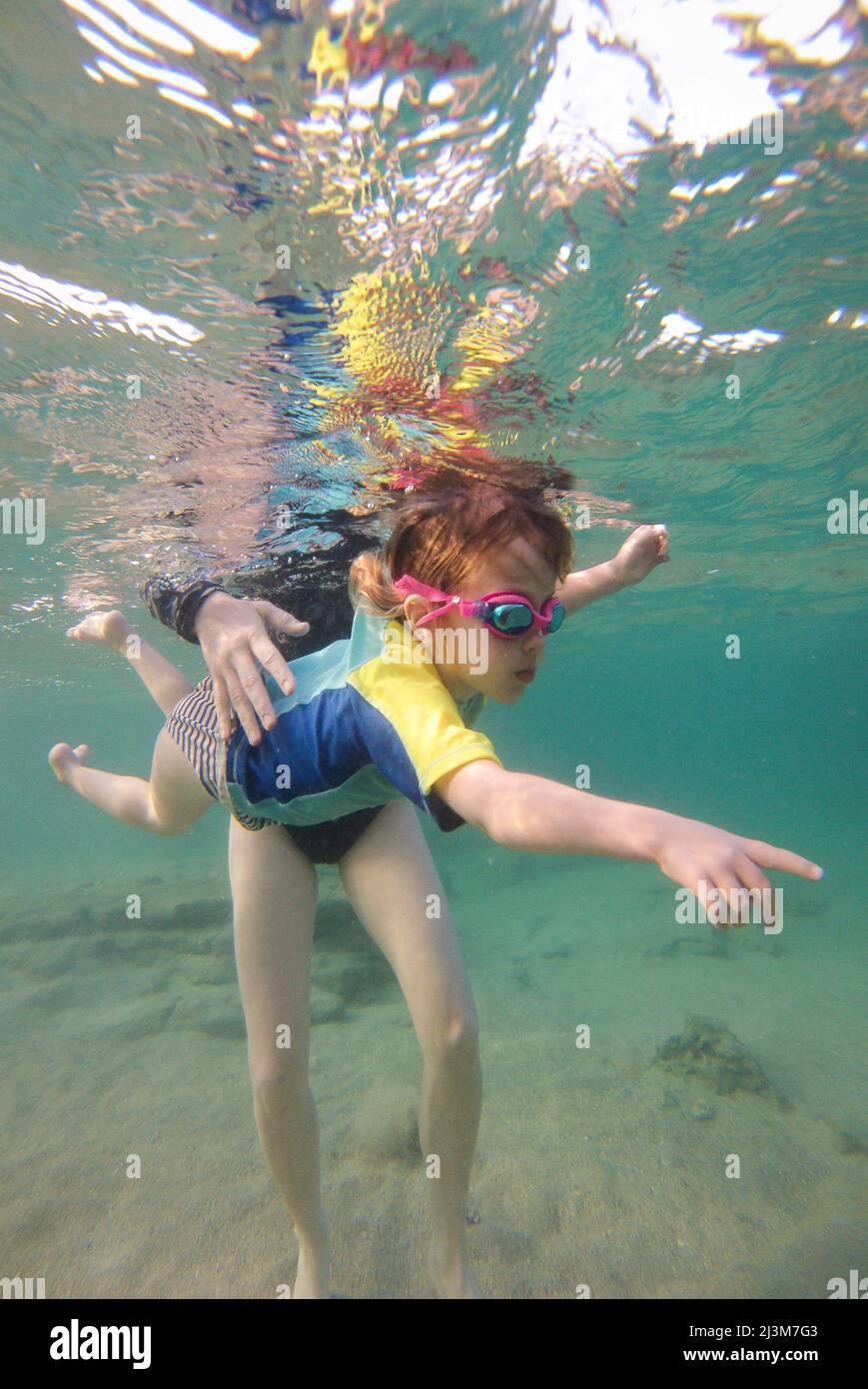 A three year old girl pointing as she swims underwater with her Mother.; Shacks Beach, Aquadilla, Puerto Rico. Stock Photo