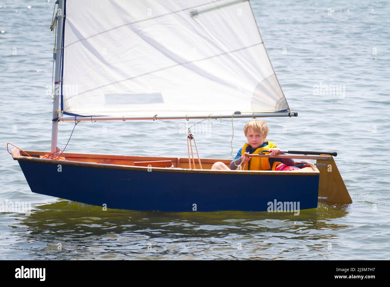 An eight year old boy sailing a small boat at summer sailing camp run