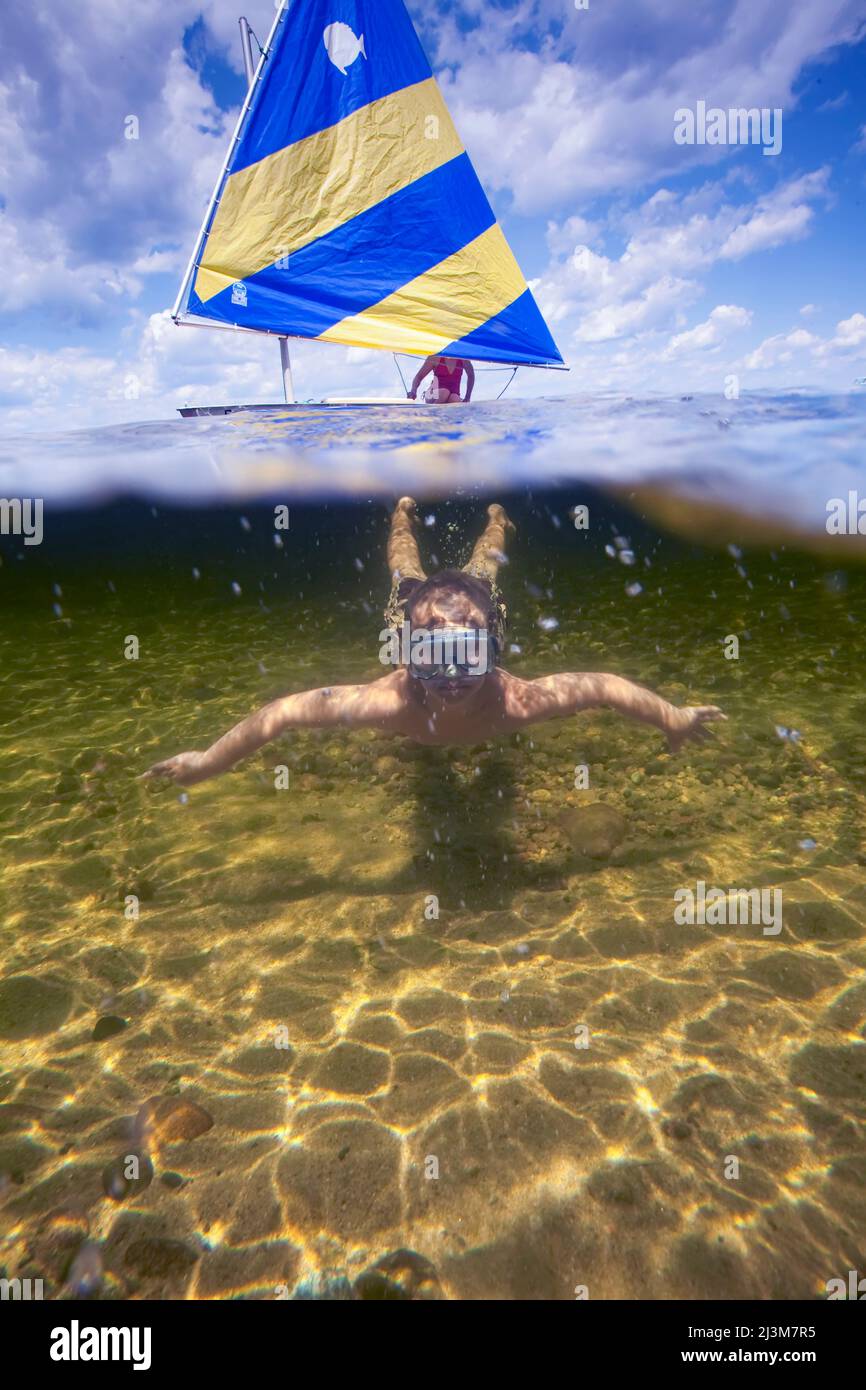 An eight year old boy swims underwater while his Mom sails by on a