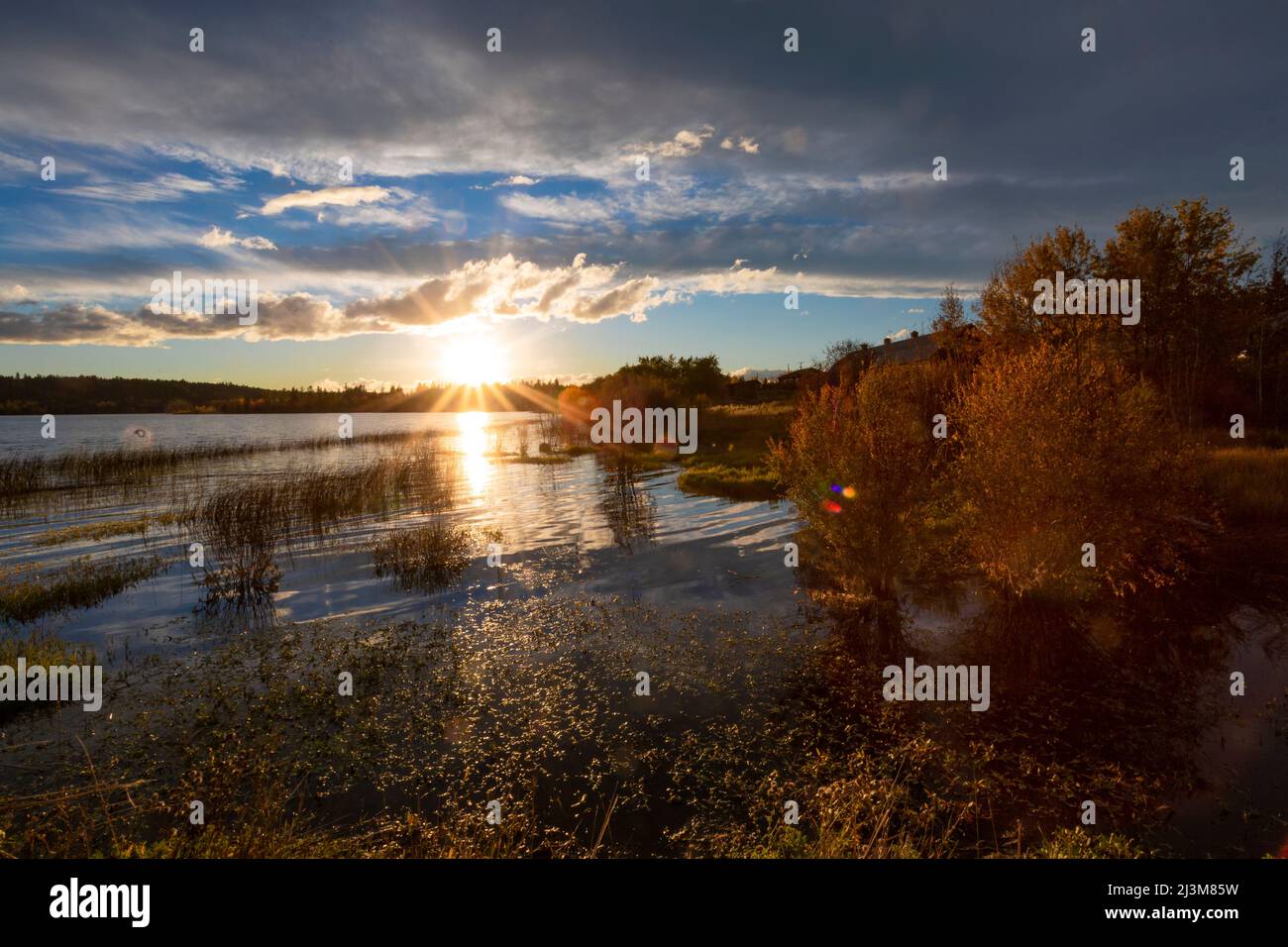 Sunburst of the setting sun over a lake in autumn; 108 Mile House, British Columbia, Canada Stock Photo