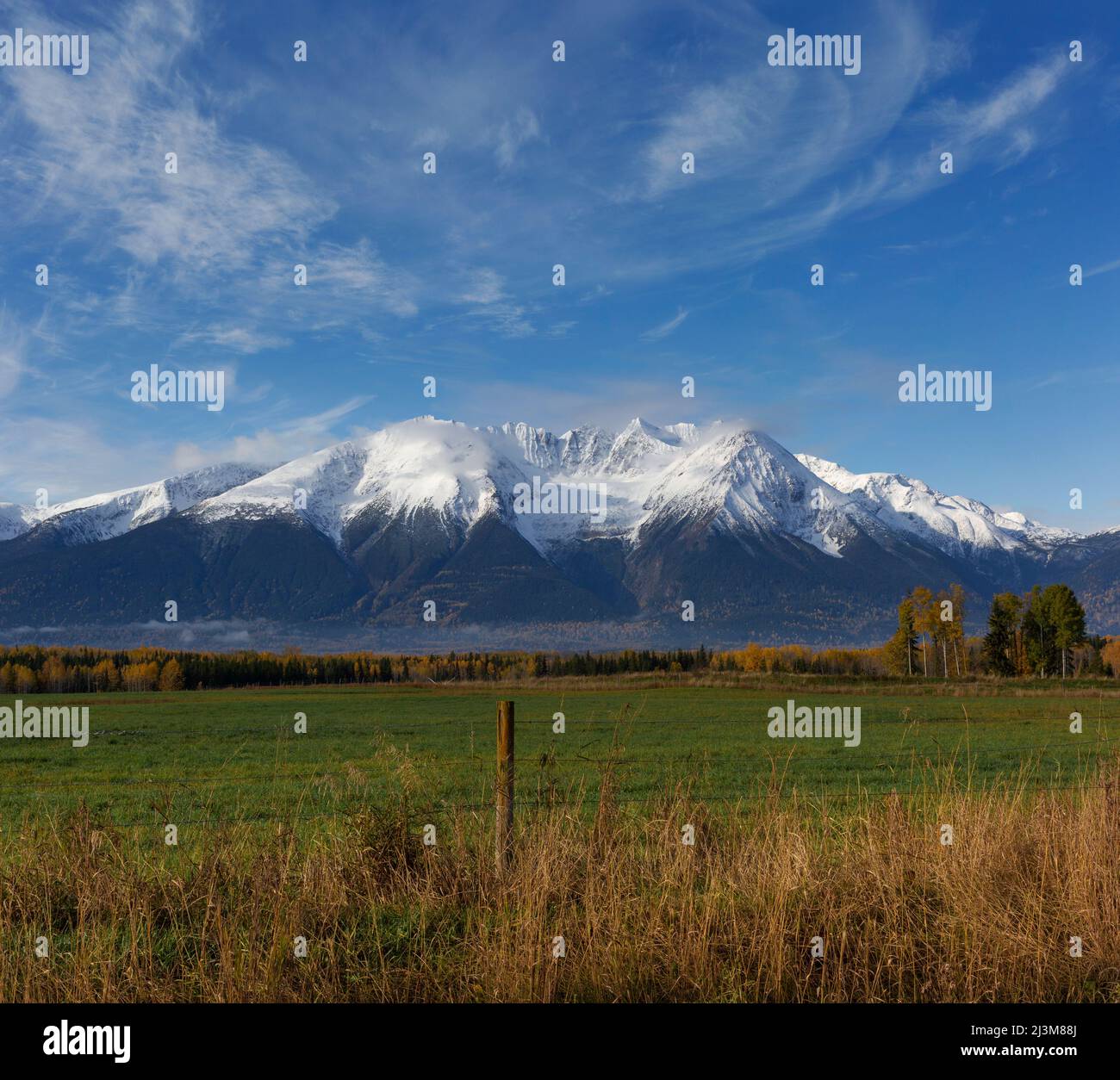 Rugged peaks of a snow-capped Cascade mountain range viewed from a country road and field in Northern British Columbia; British Columbia, Canada Stock Photo