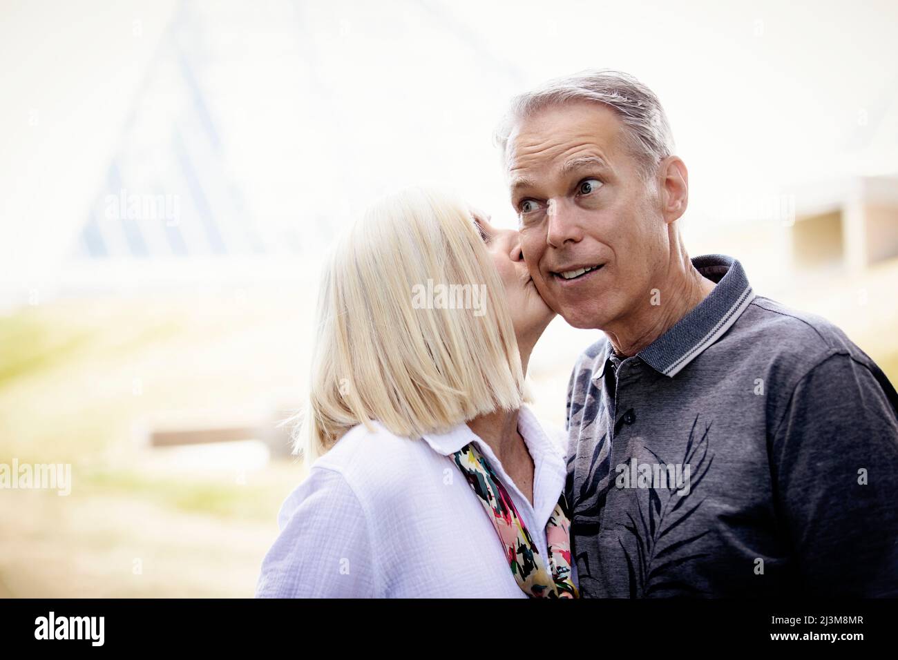 Wife kissing her husband's cheek as he has a look of surprise on his face; Edmonton, Alberta, Canada Stock Photo