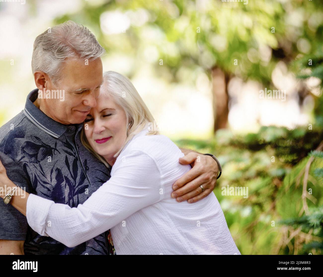 Mature couple sharing an embrace while walking outdoors on a park trail; Edmonton, Alberta, Canada Stock Photo