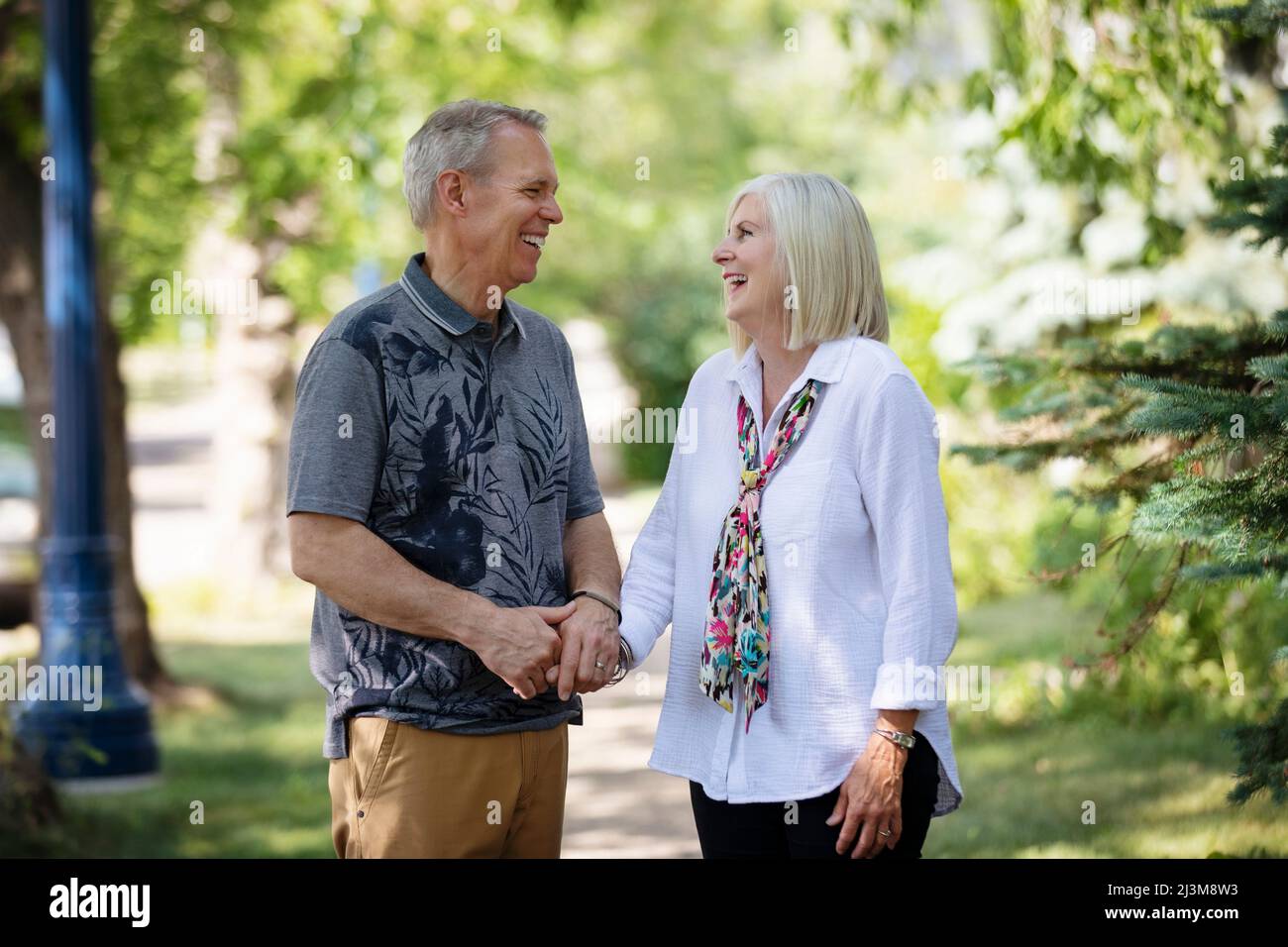 Mature couple holding hands and sharing a moment together in laughter while walking outdoors on a park trail; Edmonton, Alberta, Canada Stock Photo