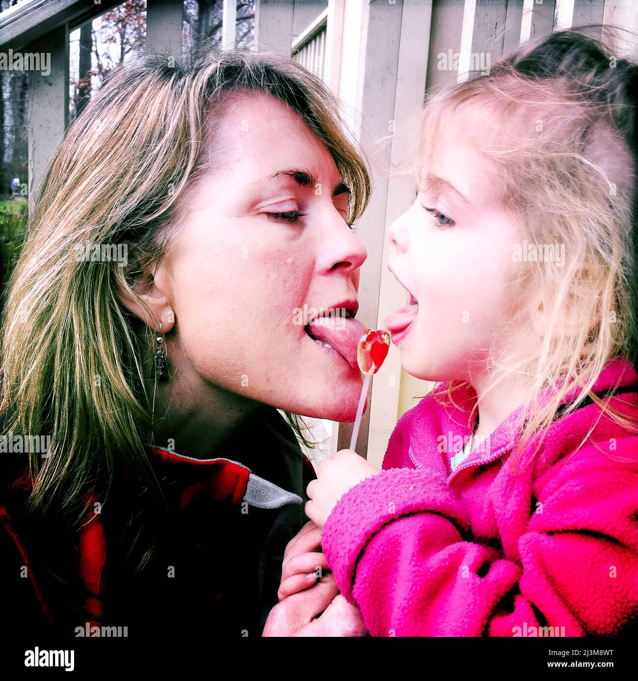 Mother and two year old daughter share a lollipop on Valentines Day.; Cabin John, Maryland. Stock Photo