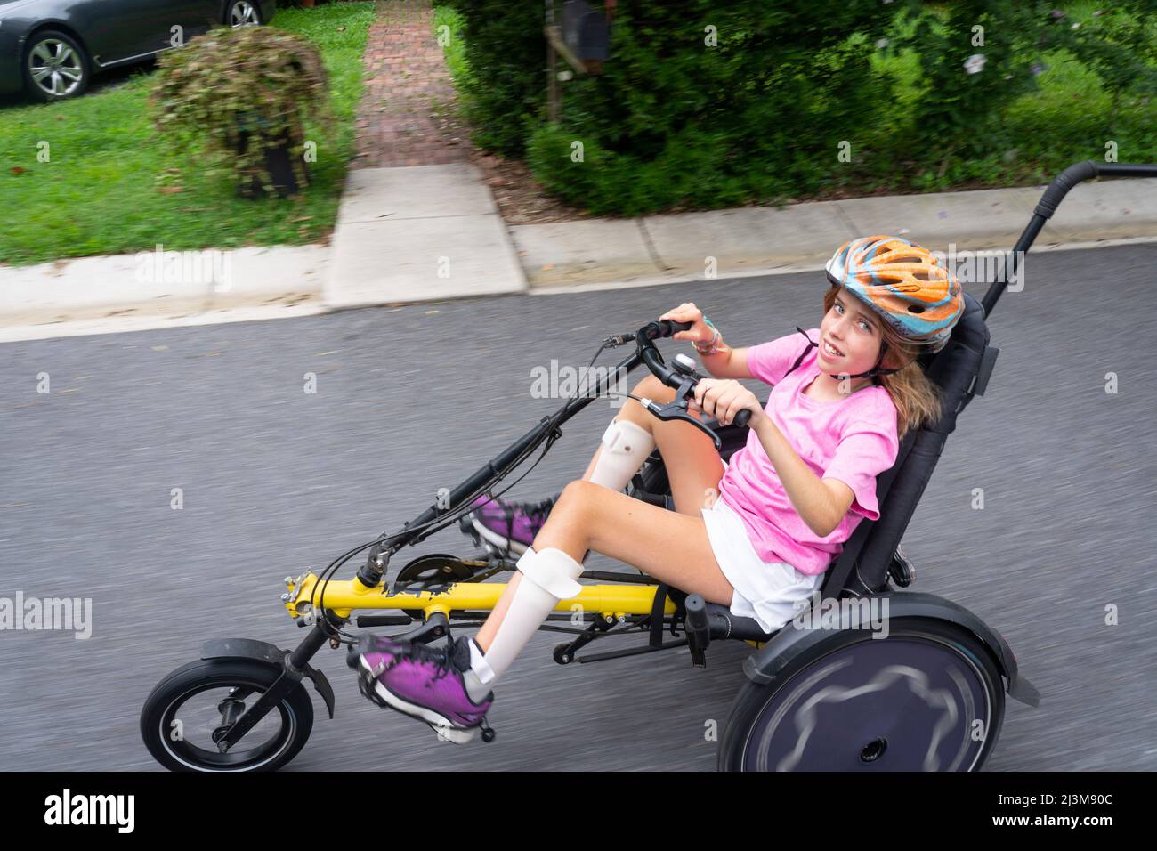 Girl with Ullrich Congenital Muscular Dystrophy riding her recumbent trike bicycle on the street near her home Stock Photo