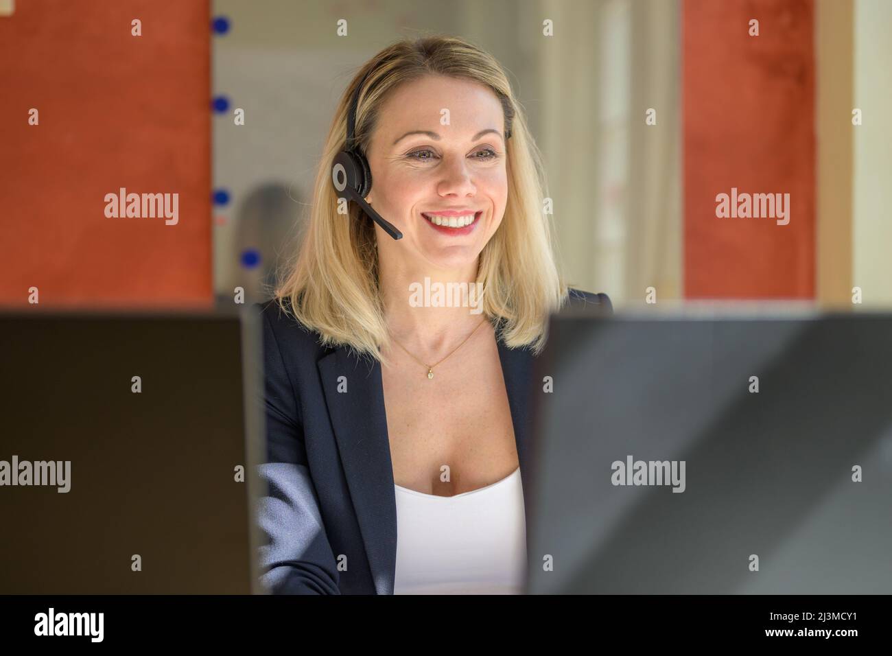 Successful female entrepreneur working on desktop computer while using a headset for conversation in modern office Stock Photo