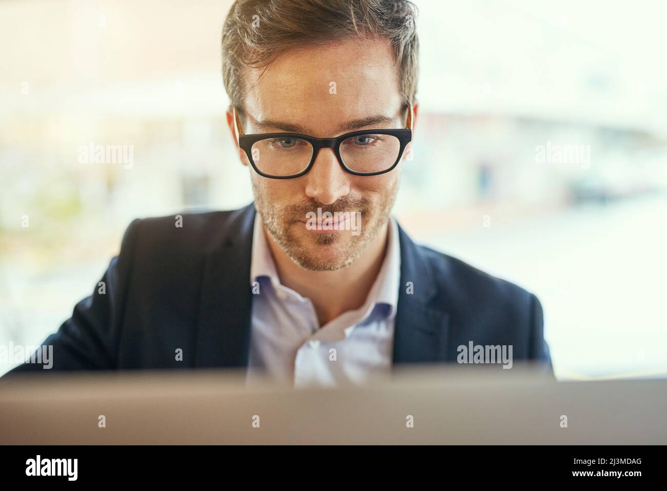 He seems quite pleased with himself. Shot of a young businessman using his laptop while sitting in a coffee shop. Stock Photo