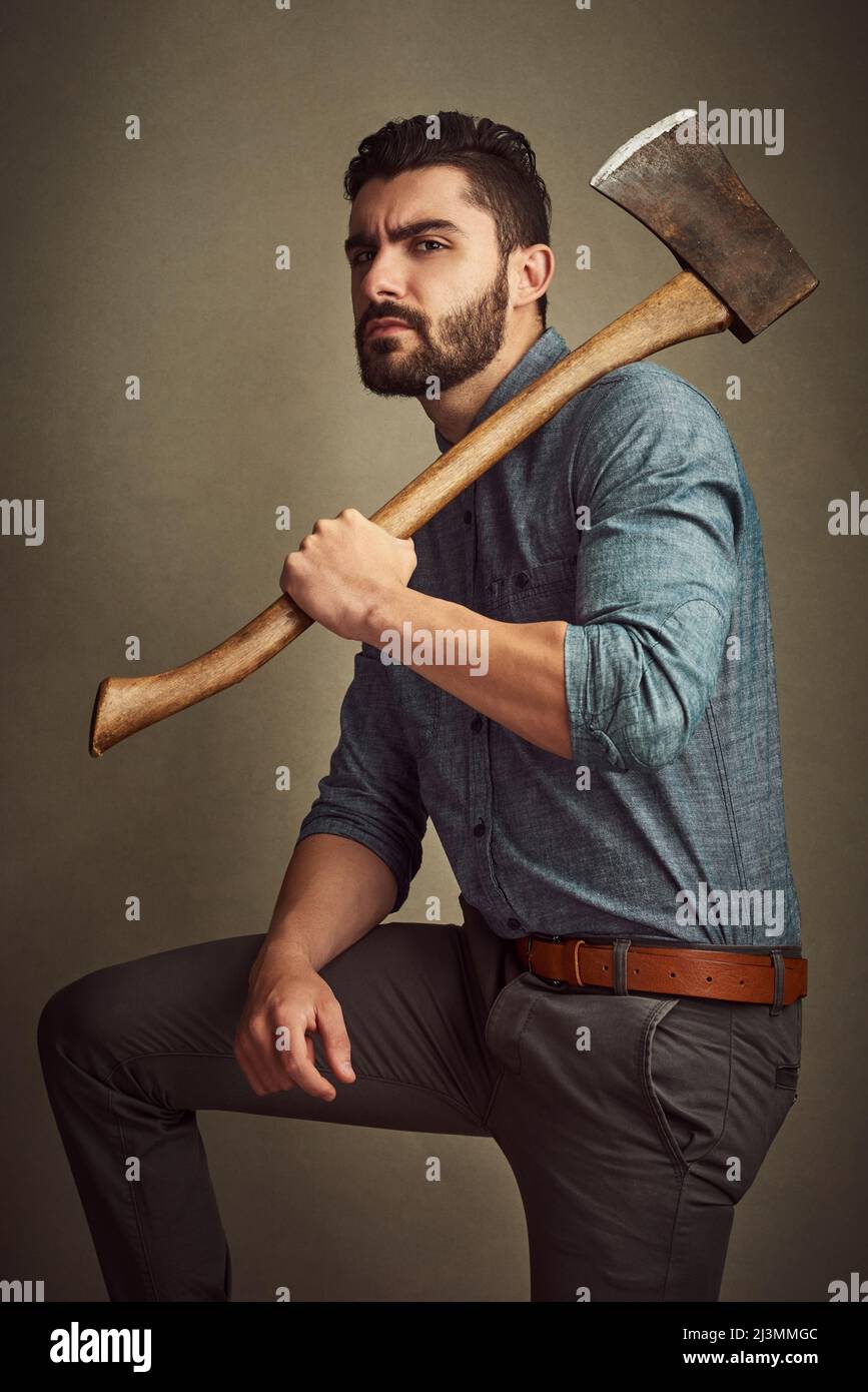 Fashionable with the right amount of rugged. Studio shot of a young man posing with an axe against a green background. Stock Photo