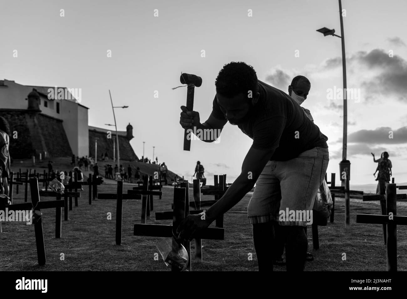 Salvador, Bahia, Brazil - October 01, 2021: Silhouette of a man fixing crosses on the ground in honor of those killed by covid-19. Barra Lighthouse, S Stock Photo