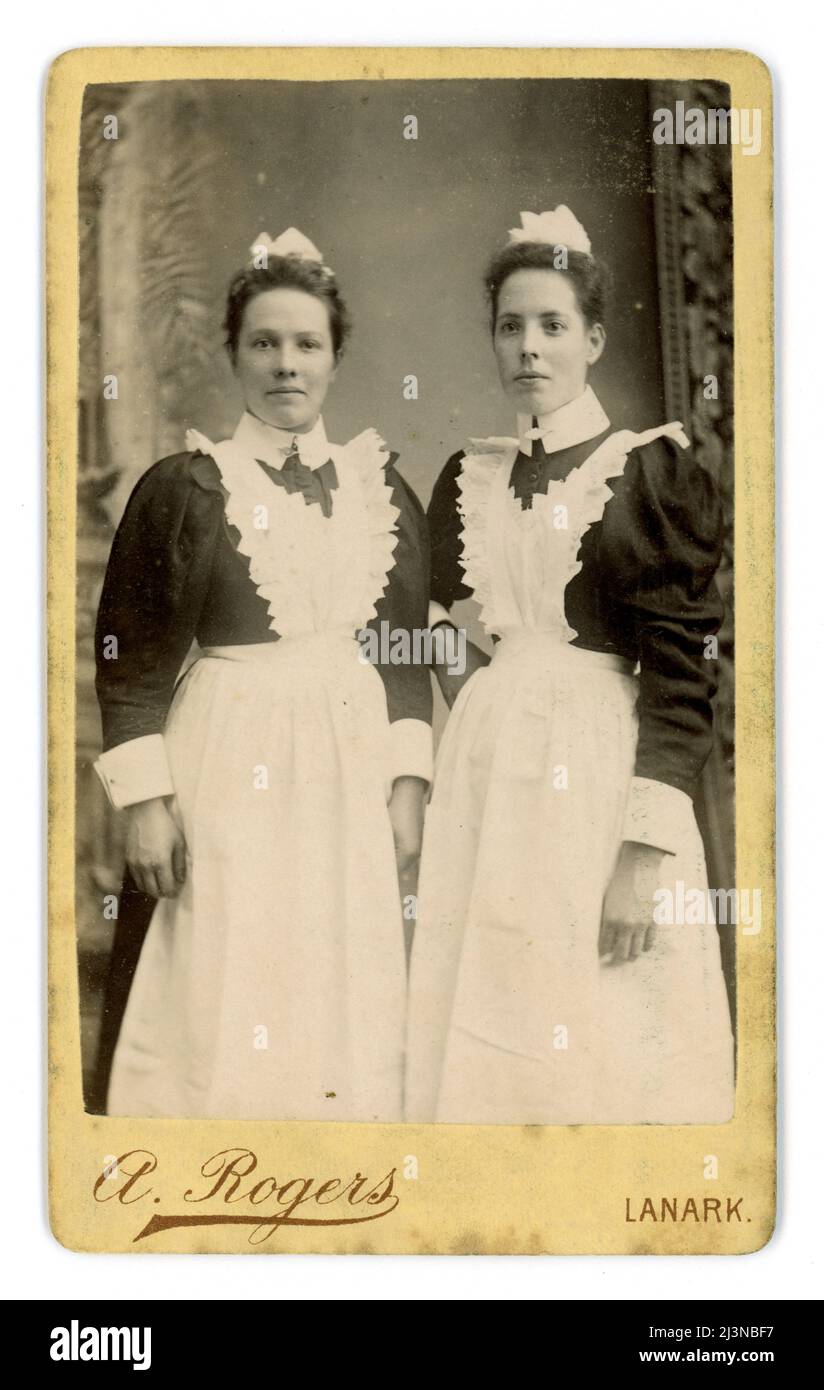 Original and clear Victorian CDV (Carte de Visite or visiting card) of 2 / two attractive, Victorian maids, Victorian servant,  wearing starched white aprons, caps, blouses with the 'leg of mutton sleeves' fashionable in the mid 1890's. From the photographic studio of Archibald Rogers, Lanark, South Lanarkshire (Clydesdale) Scotland, U.K. Circa 1895 Stock Photo