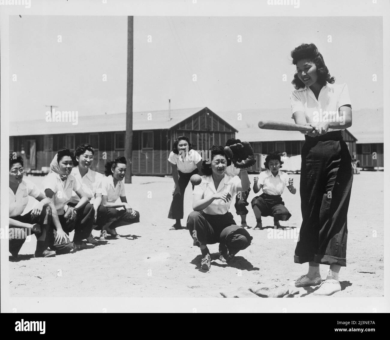 Japanese relocation, California. Maye Noma, behind the plate, and Tomi Nagao, at bat, in a practice game between members of the Chick-a-dee softball team, which was kept intact when the players were evacuated from Los Angeles to Manzanar, California, a War Relocation Authority Center for evacuees of Japanese ancestry. Stock Photo