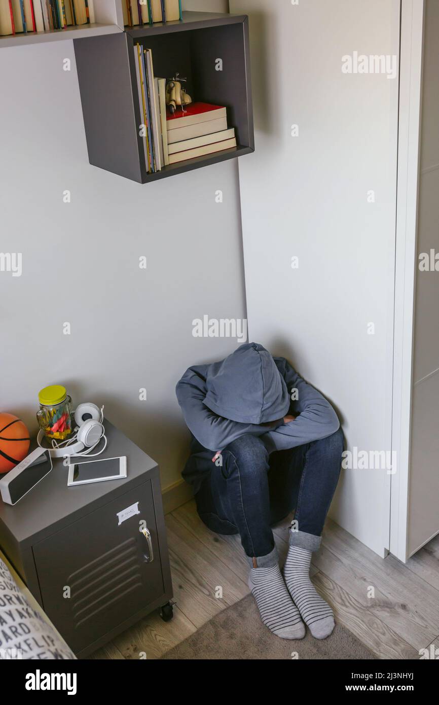 Teenager boy with anxiety sitting on the floor of his bedroom with his