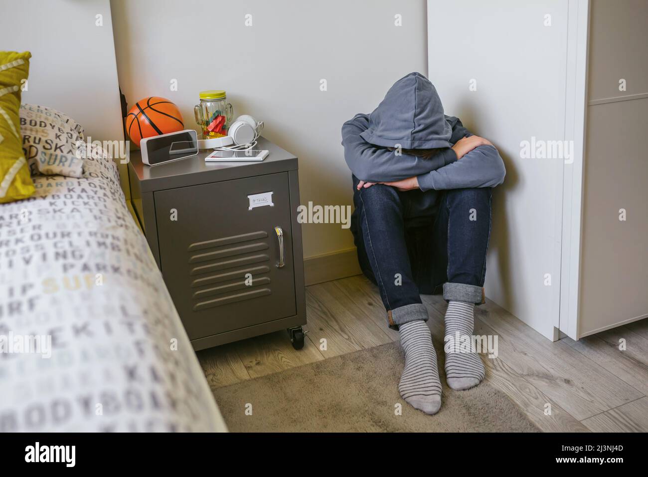 Teenager boy with anxiety sitting on the floor of his bedroom with his