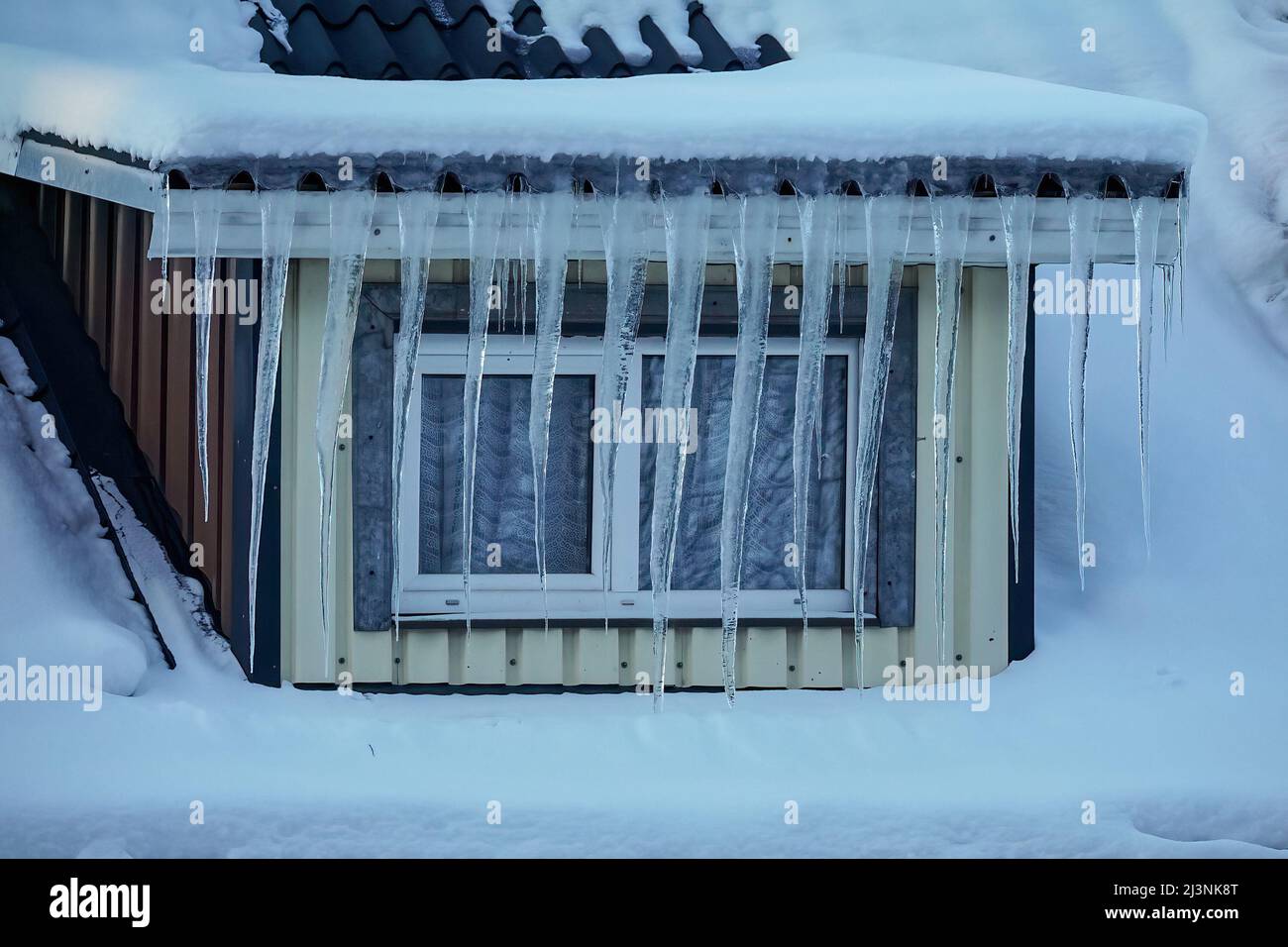 Long transparent icicles hanging from the roof in front of the window of house Stock Photo