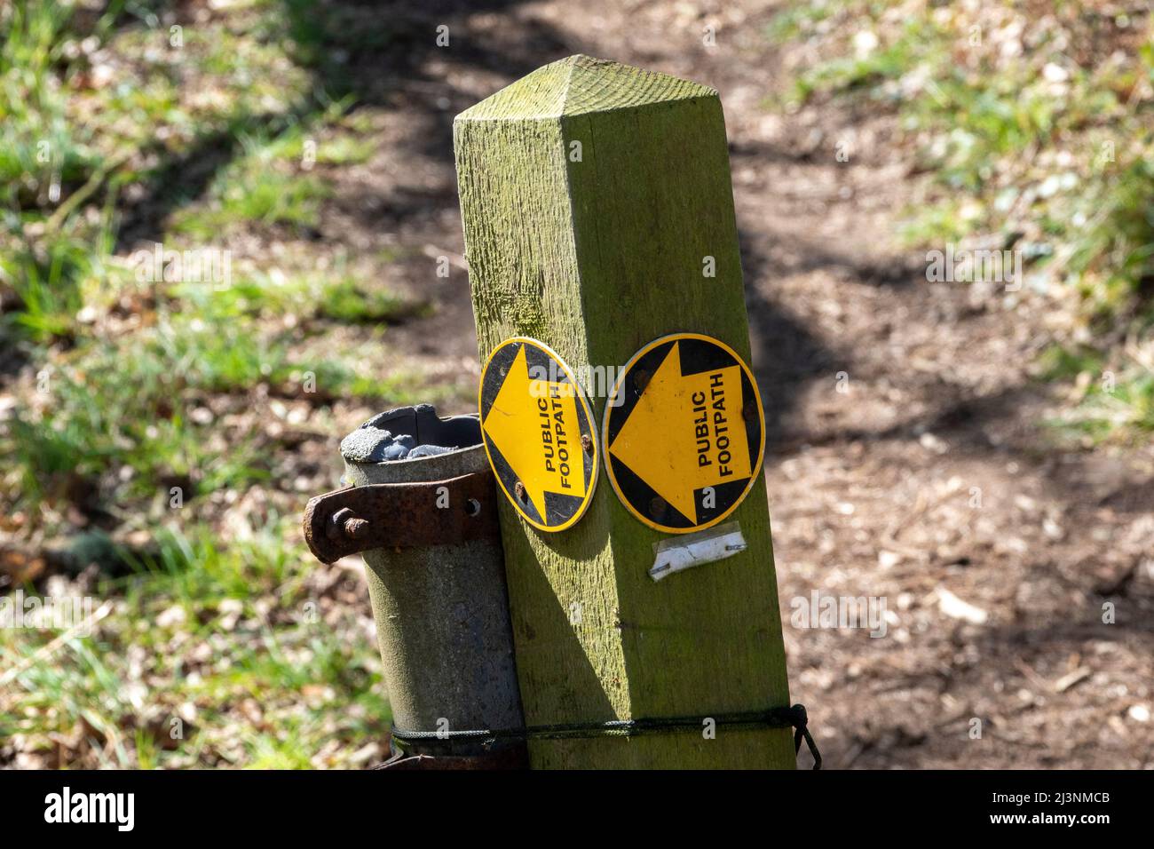 A single wooden post with a yellow arrow footpath sign disc on two faces indicating left Stock Photo