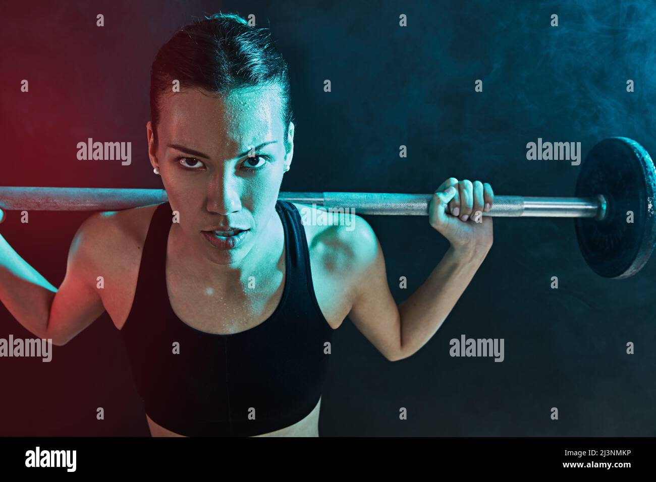 I believe in redefining my impossible. Shot of a young woman lifting weights against a dark background. Stock Photo