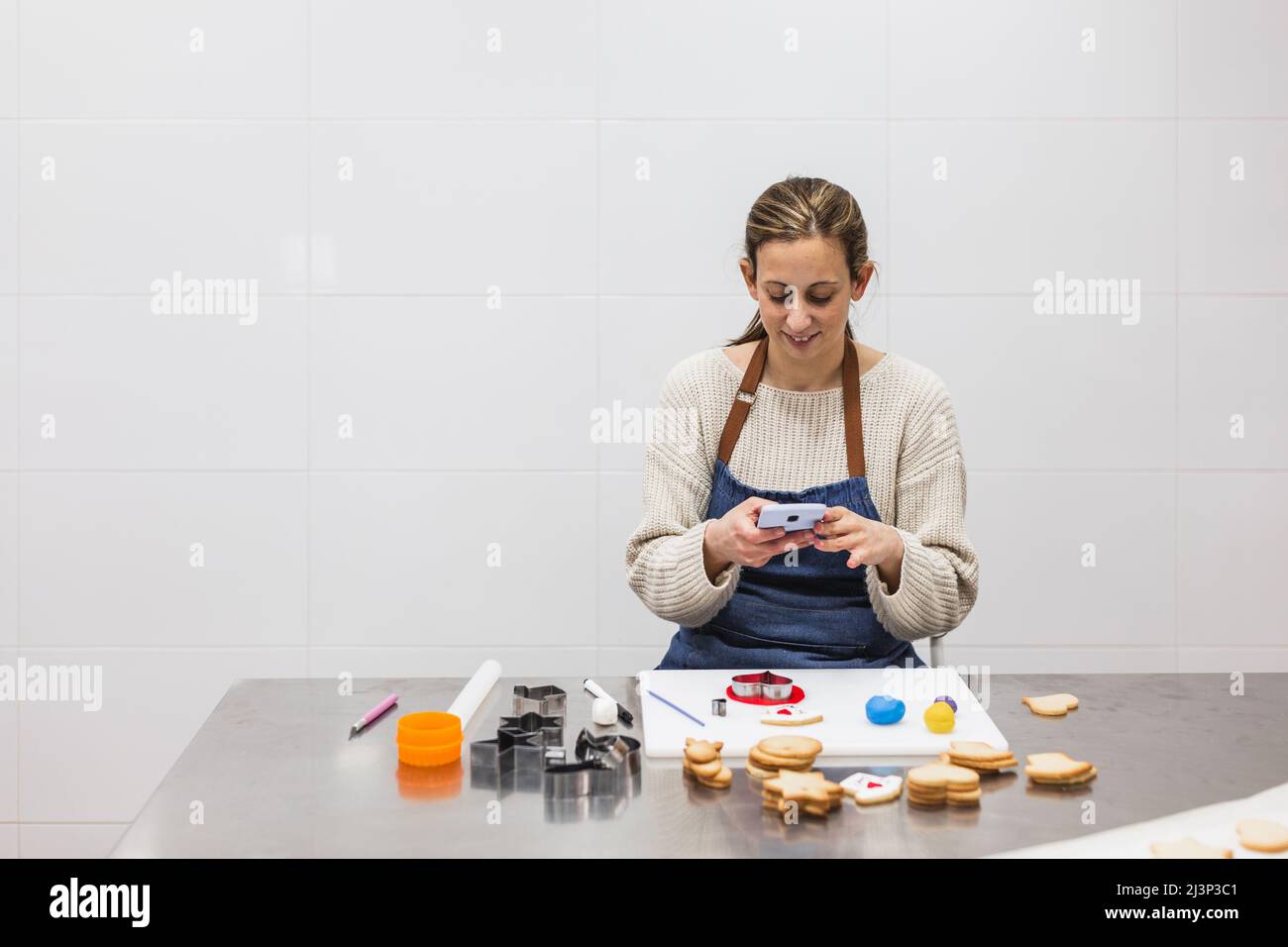 Female pastry chef using her mobile phone while working in the kitchen