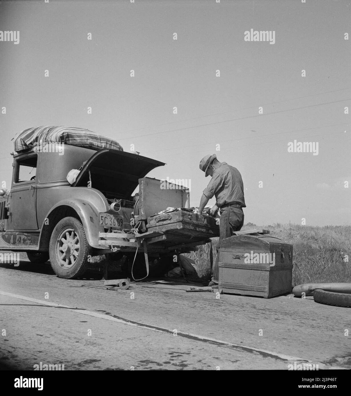 Car trouble on west side, Highway no. 33. In San Joaquin Valley. Formerly a California cowhand and roving laborer, now with wife, he follows the fruit. &quot;My uncle homesteaded here sixty years ago. I'm lower on money than at any time&quot;. Stock Photo