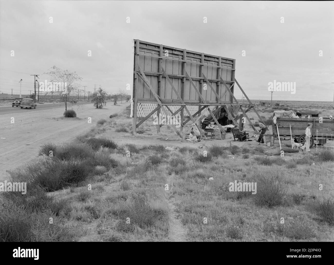 Three families camped on the plains along U.S. 99 in California. They are camped behind a billboard which serves as a partial windbreak. All are in need of work. Stock Photo