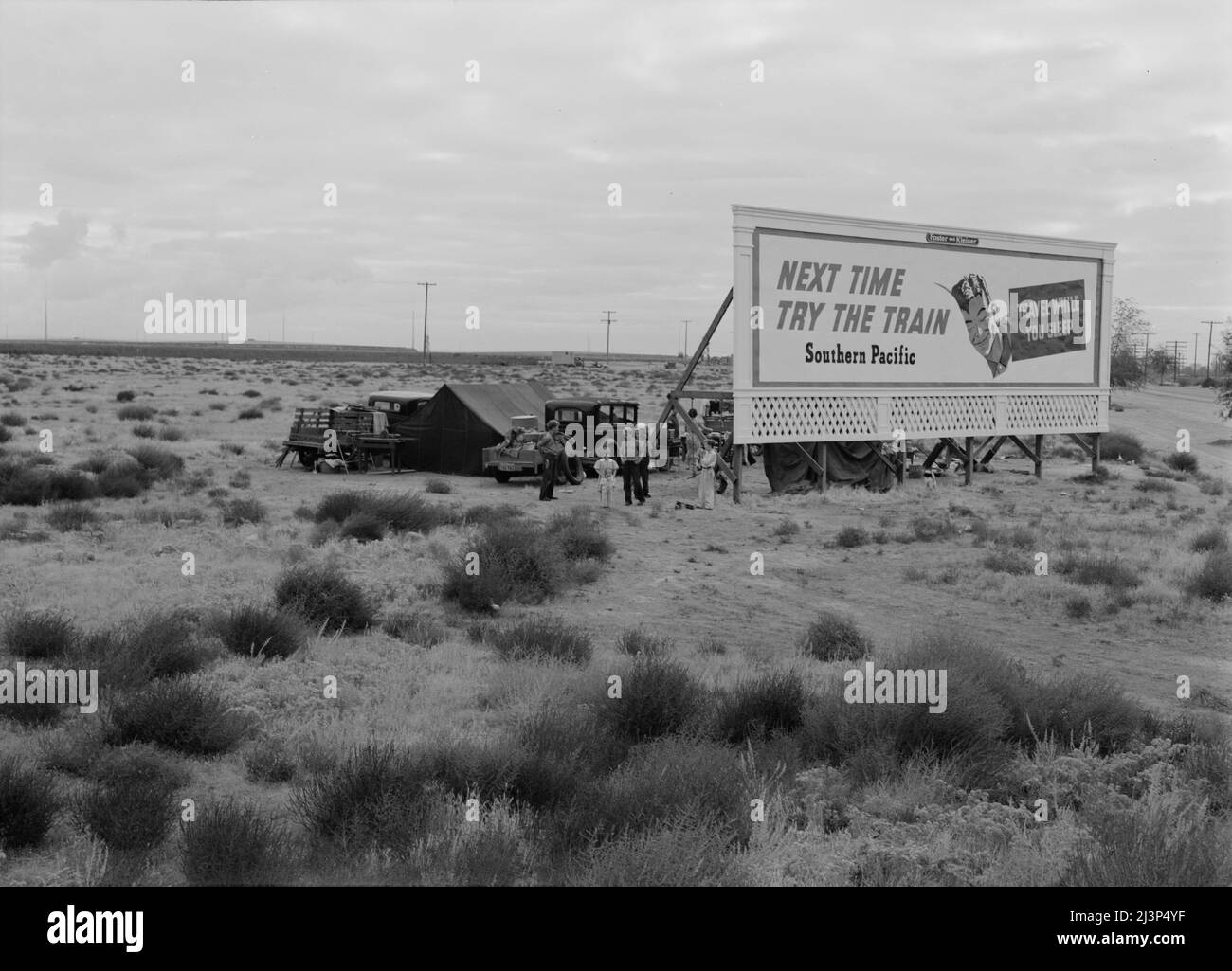 Three families camped on the plains along U.S. 99 in California. They are camped behind a billboard which serves as a partial windbreak. All are in need of work. Stock Photo
