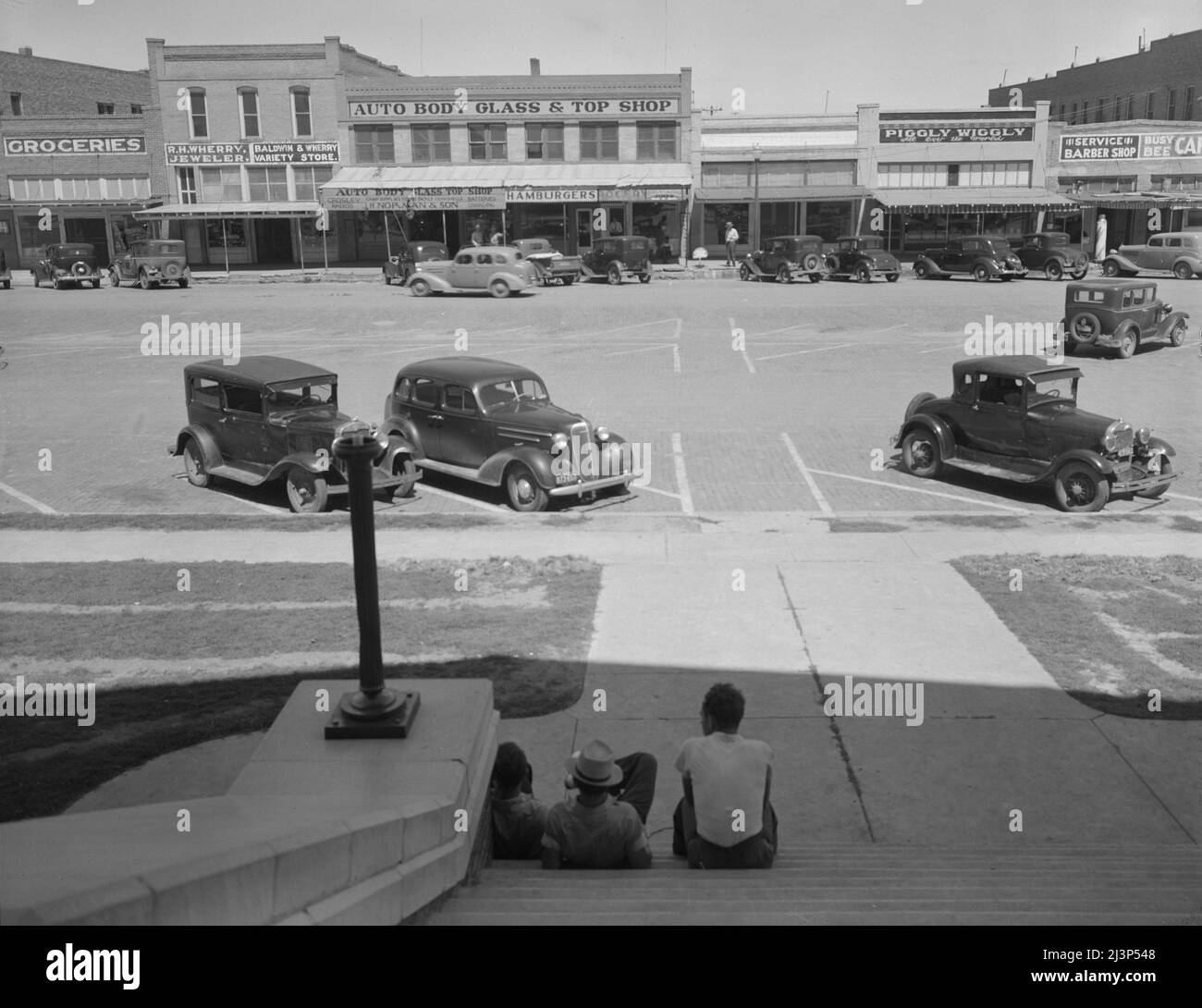 The town square of Memphis, Texas. [Grocery store, jeweller's, 'Auto Body Glass &amp; Top Shop', burger shop, Piggly Wiggly, barber's shop]. Stock Photo