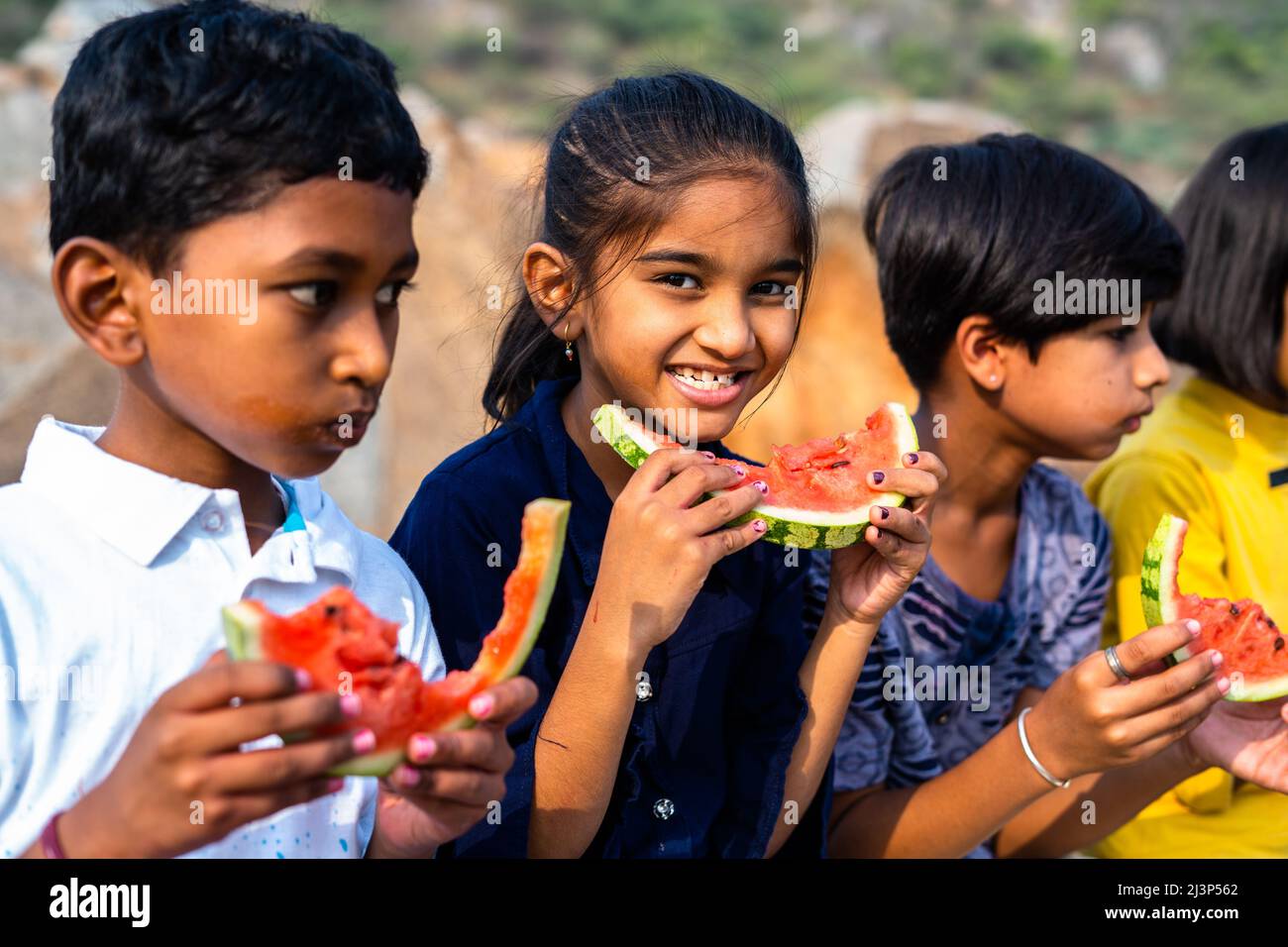 girl kid looking camera while group of kids busy eating watermelon during hot summer day - concept of dehydration, healthy eating and friendship Stock Photo