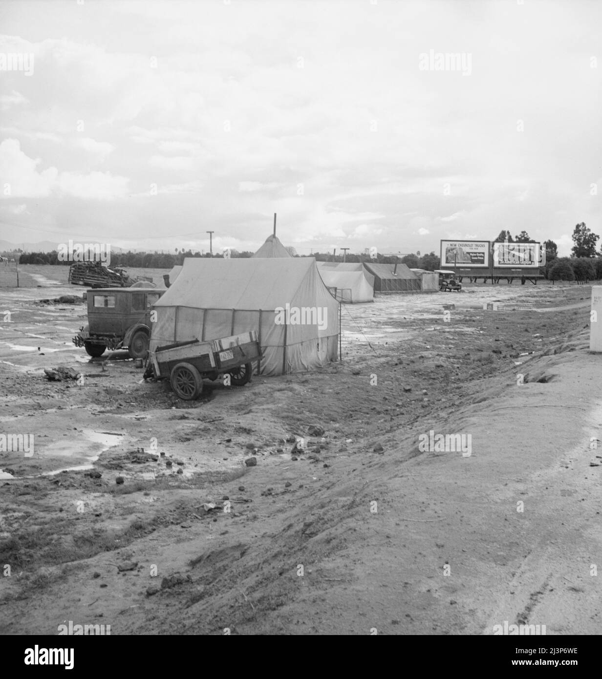 Tulare County. Winter quarters, migratory agricultural workers. Beside the highway. Tulare County, California. [Signs: 'New Chevrolet Trucks for 1939 - Higher Quality - Lower Prices'; ...'for Enduring Peace - The American Legion - 20th Anniversary']. Stock Photo