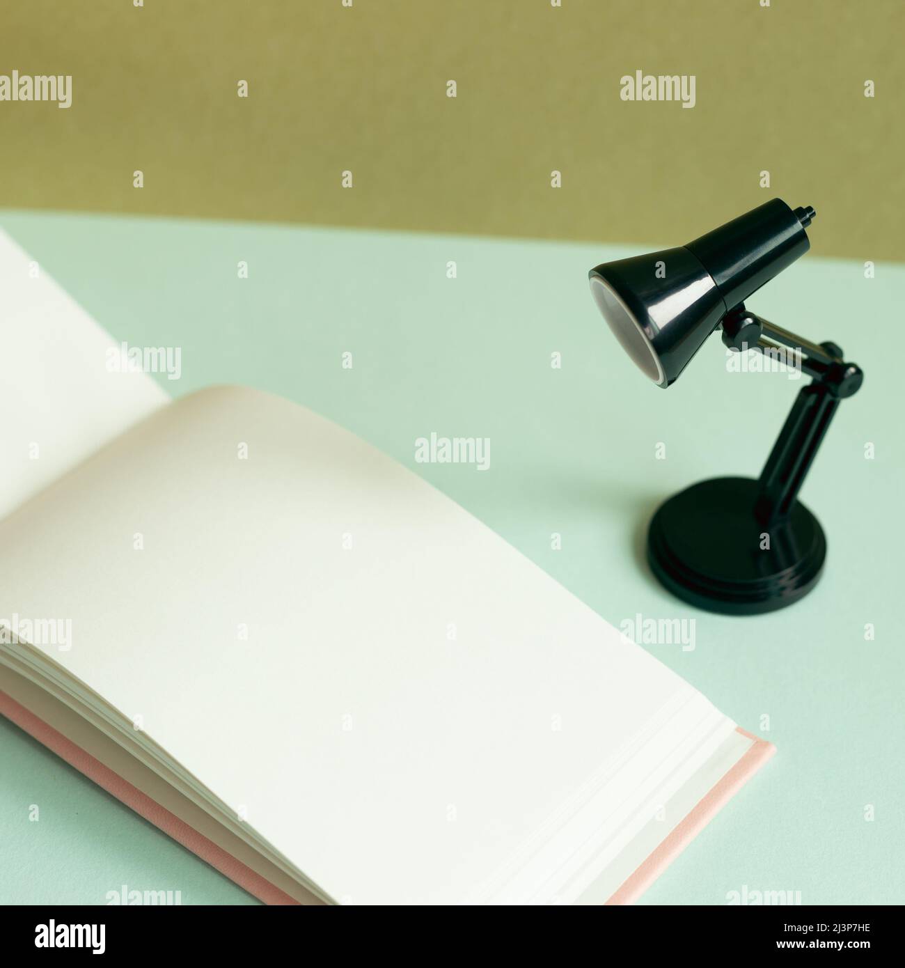 Blank notebook and black desk lamp on sky blue desk. khaki wall background Stock Photo