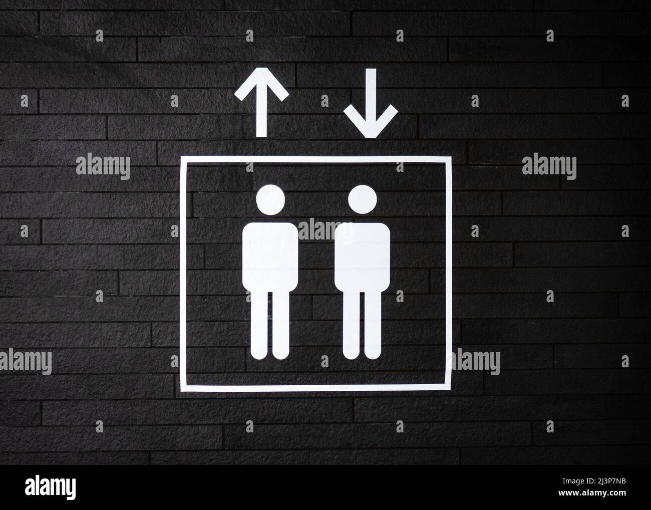 Clean lines lift symbol sign going up and down in white paint on dark black textured wall. Two symbols of men standing in elevator. Stock Photo