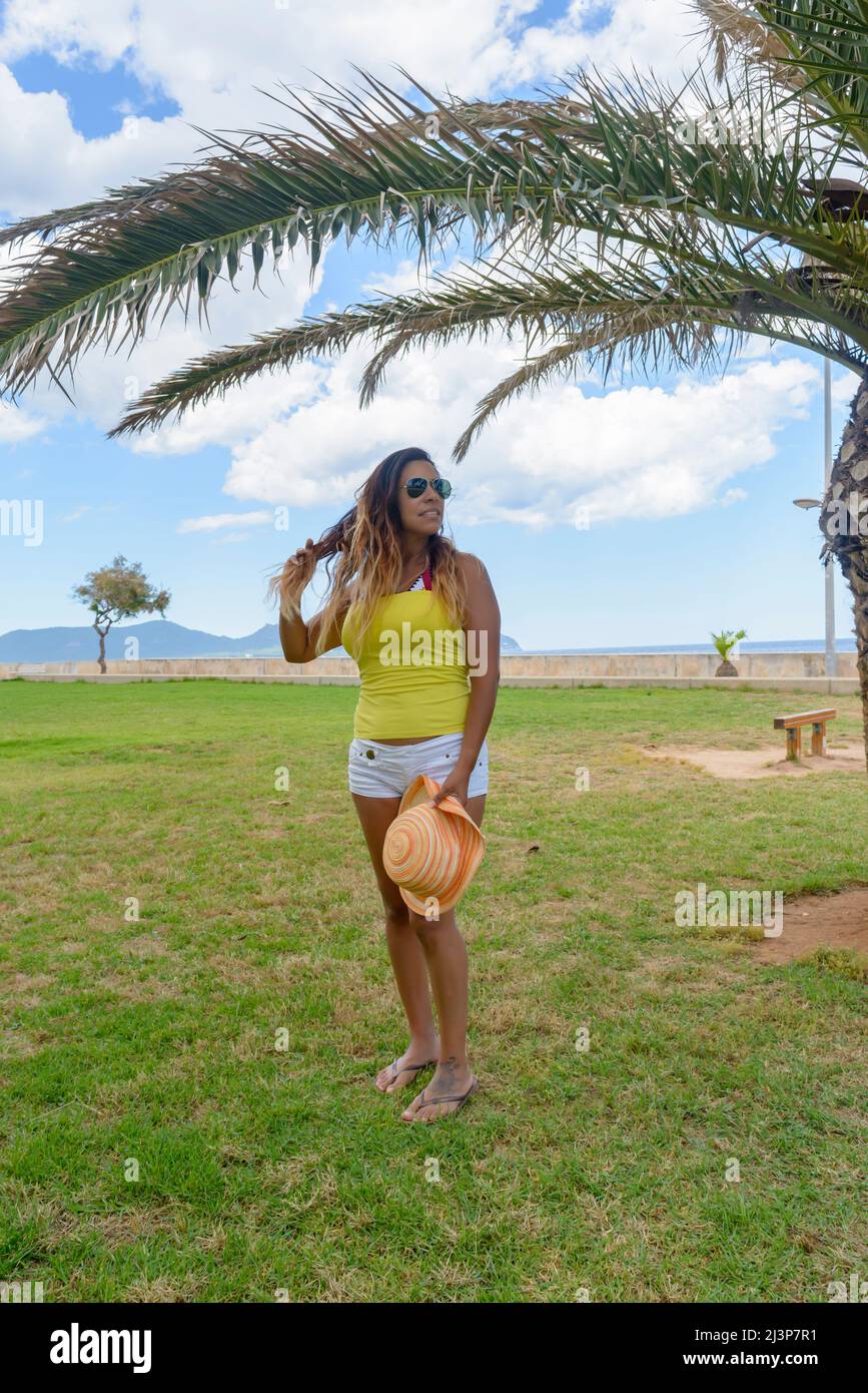 portrait of a latin woman smiling, having fun, on vacation in mallorca posing on a warm spring summer day, under a palm tree, hollidays concept Stock Photo
