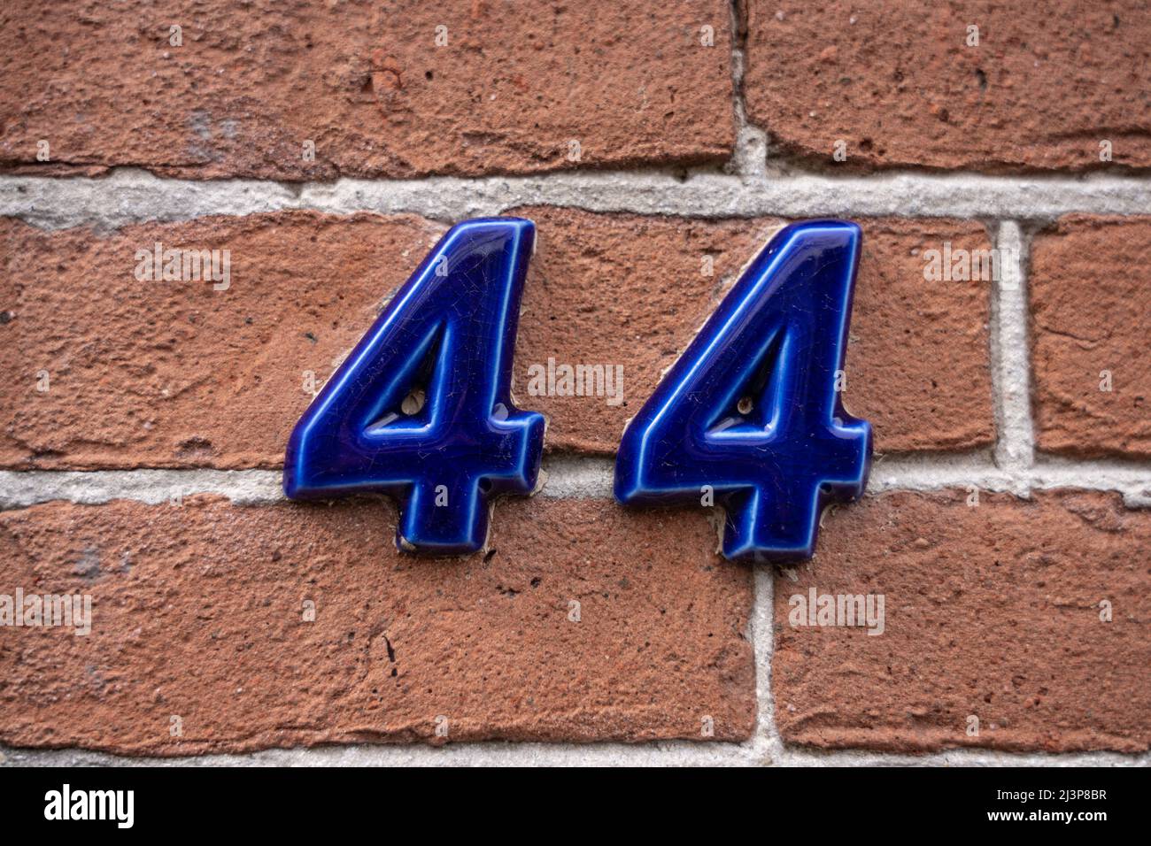 The number 44 in blue ceramic finish on red brick wall. Forty four. Stock Photo