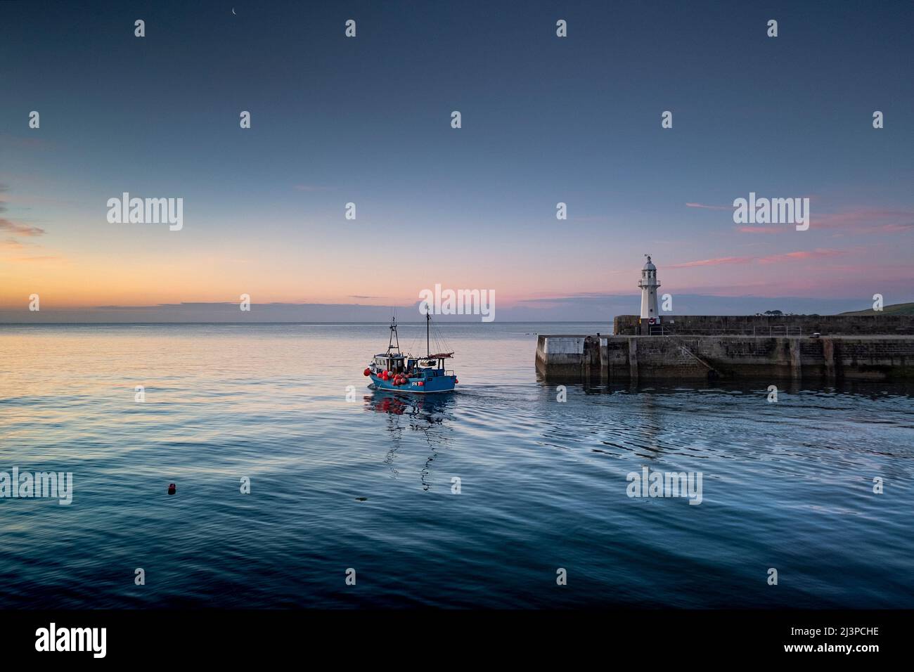 Small fishing boat leaving mevagissey harbour, cornwall at dawn with calm sea Stock Photo