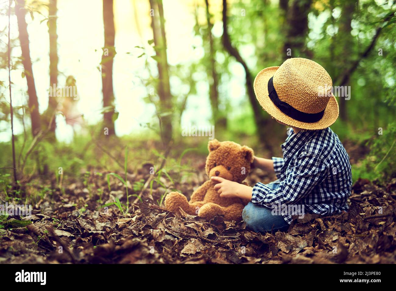 Shh Teddy, I heard something. Shot of a little boy sitting in the forest with his teddy bear. Stock Photo