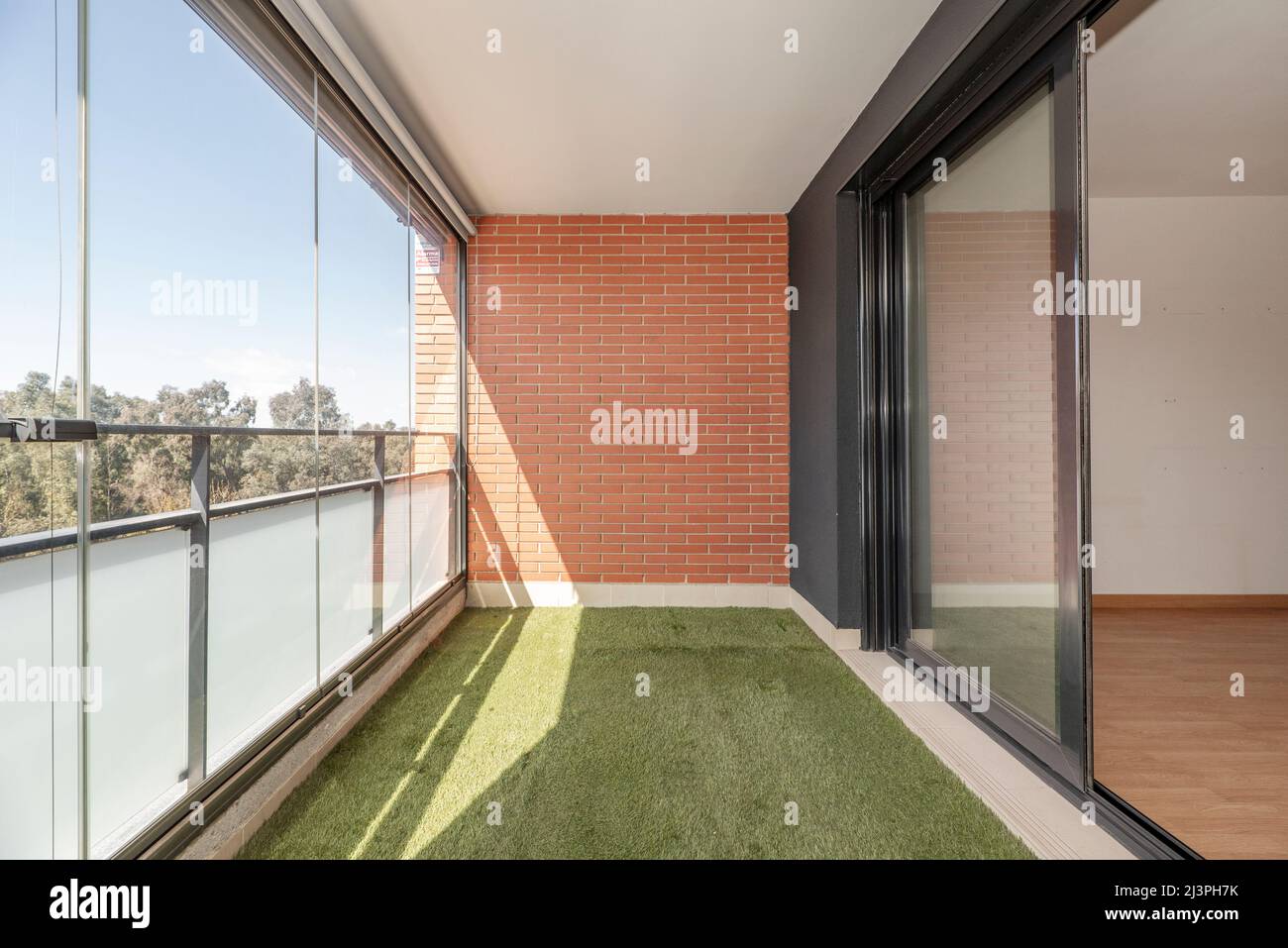 Terrace with glass wall, artificial grass floor and painted iron railing in urban residential house on a sunny spring day Stock Photo