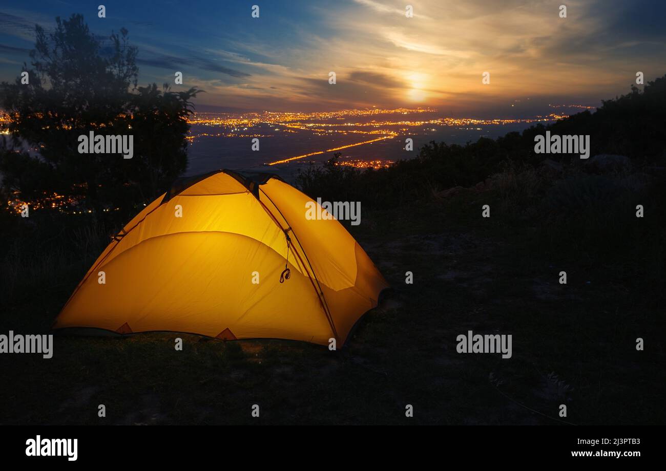 Orange tourist tent against backdrop of city lights at sunset Stock Photo